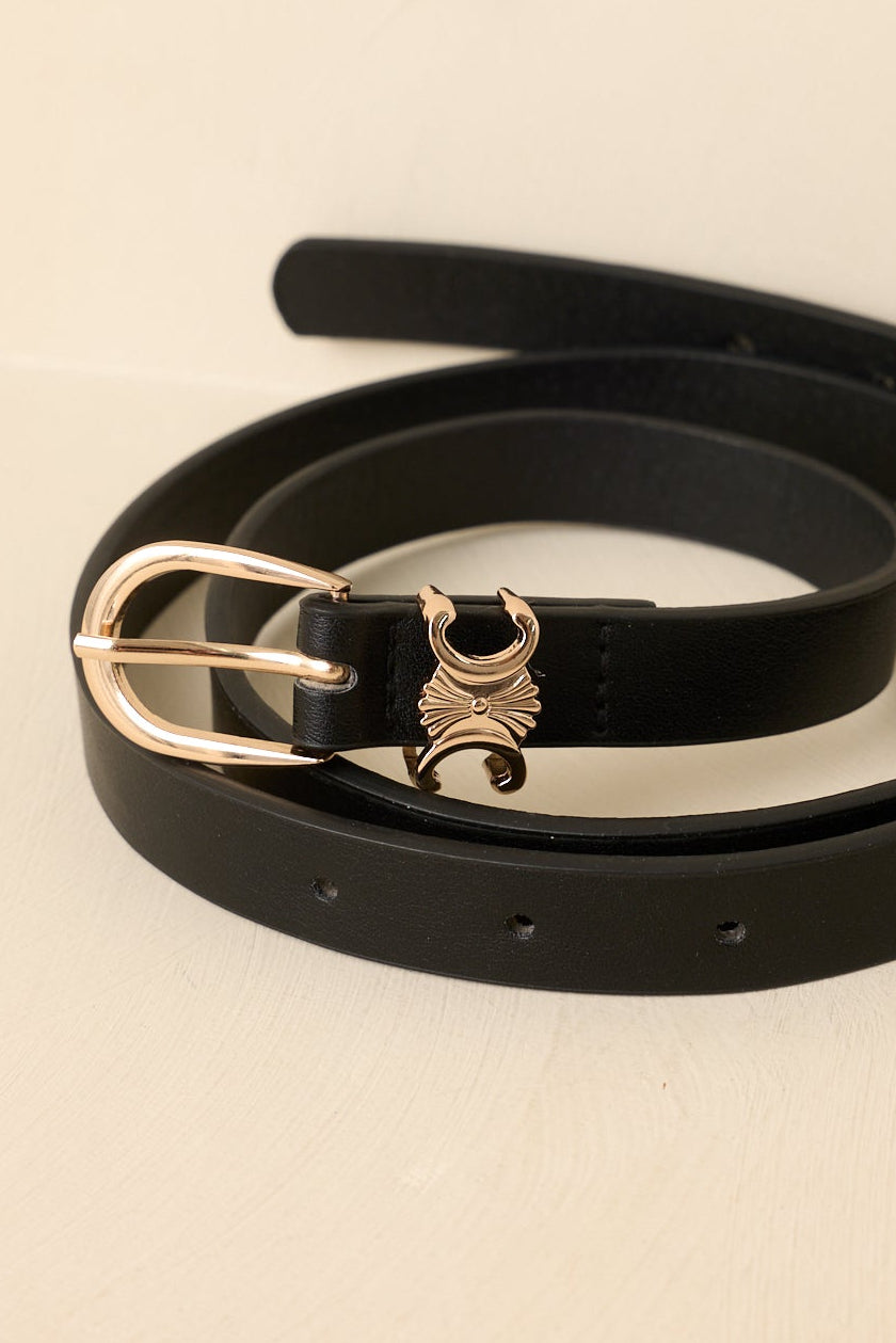Black belt with a gold buckle, curled up on a beige background.