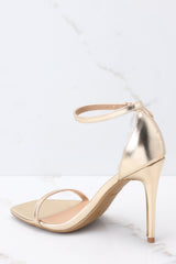 Back view of these shoes that feature an adjustable ankle strap, a thin strap over the top of the foot, and a thin heel.