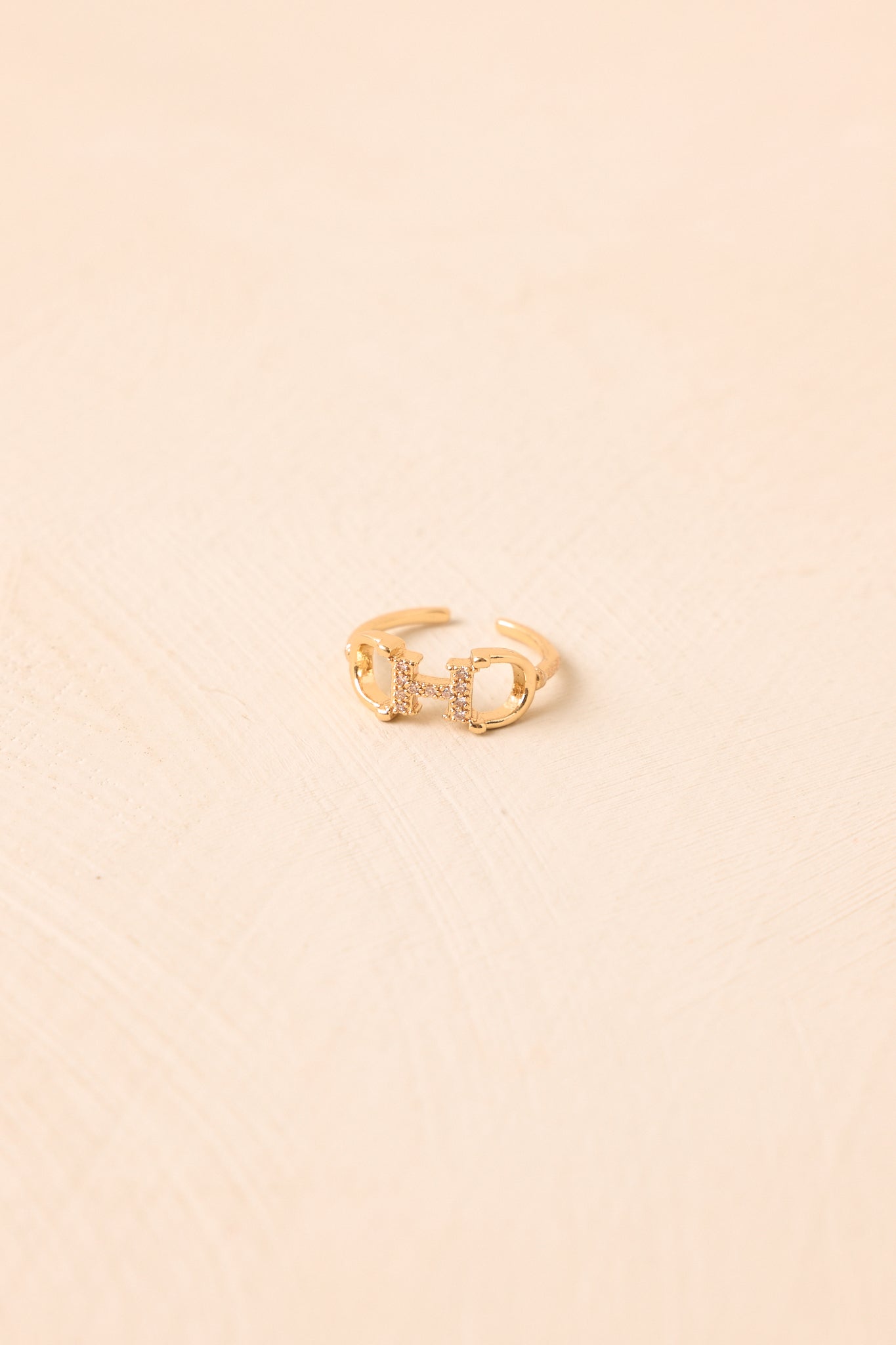 Adjustable gold-tone ring against a beige background featuring a refined horsebit centerpiece with sparkling crystal embellishments.