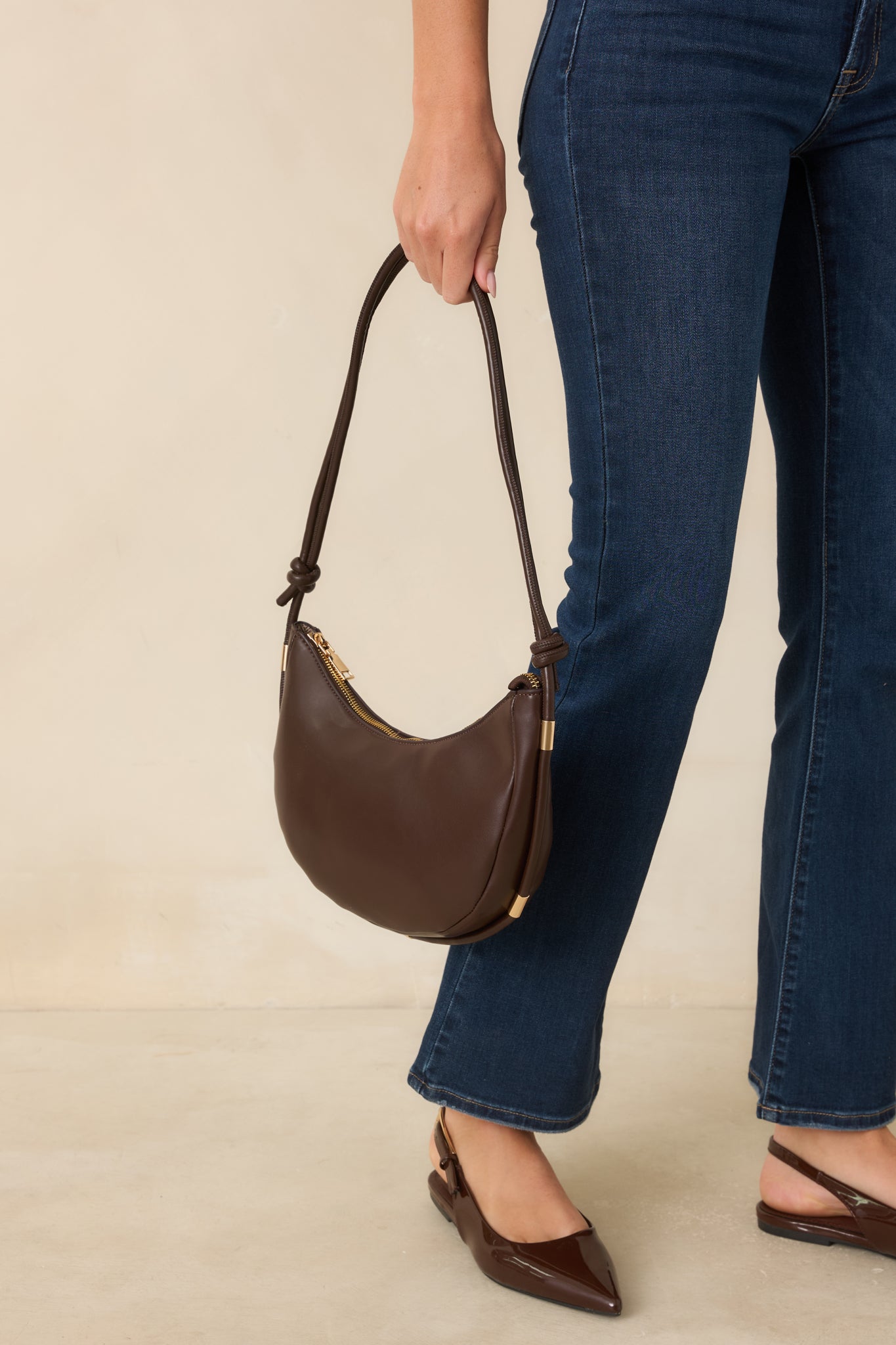 The adjustable shoulder strap highlights decorative knots and polished gold-tone hardware on this versatile handbag.