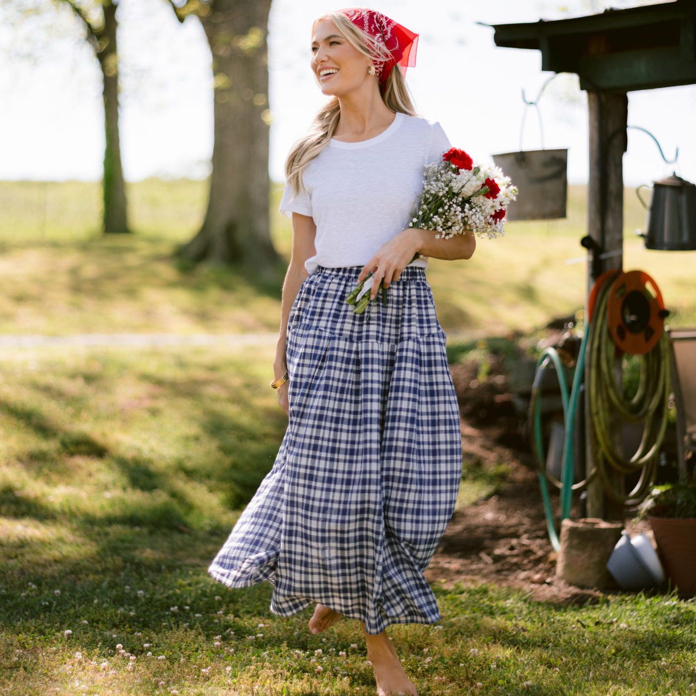 Woman in a blue plaid skirt, holding flowers and wearing a headscarf.