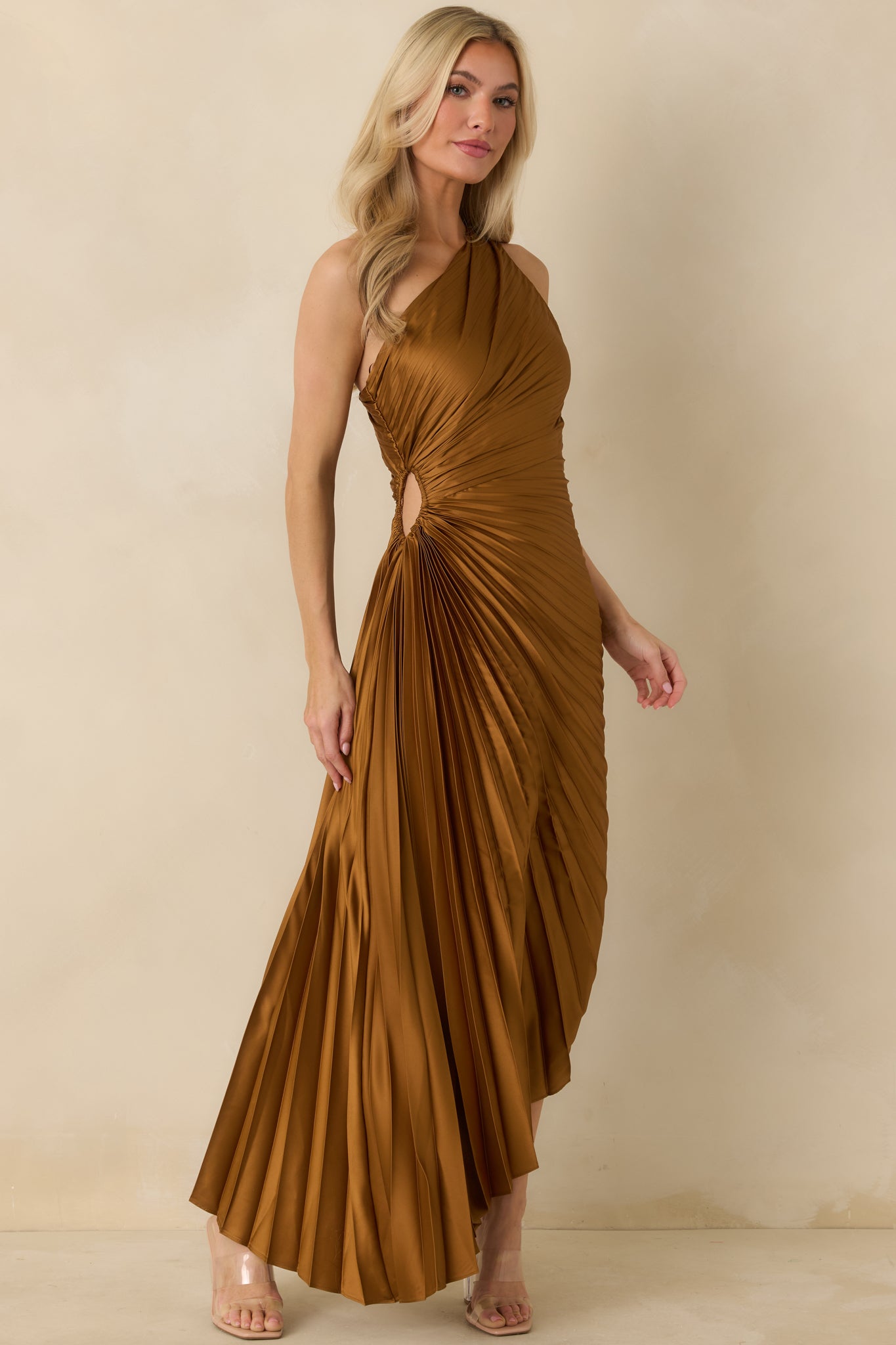 Front-facing angle of bronze maxi dress highlighting asymmetric neckline, pleated detailing, and elegant skirt hemline.