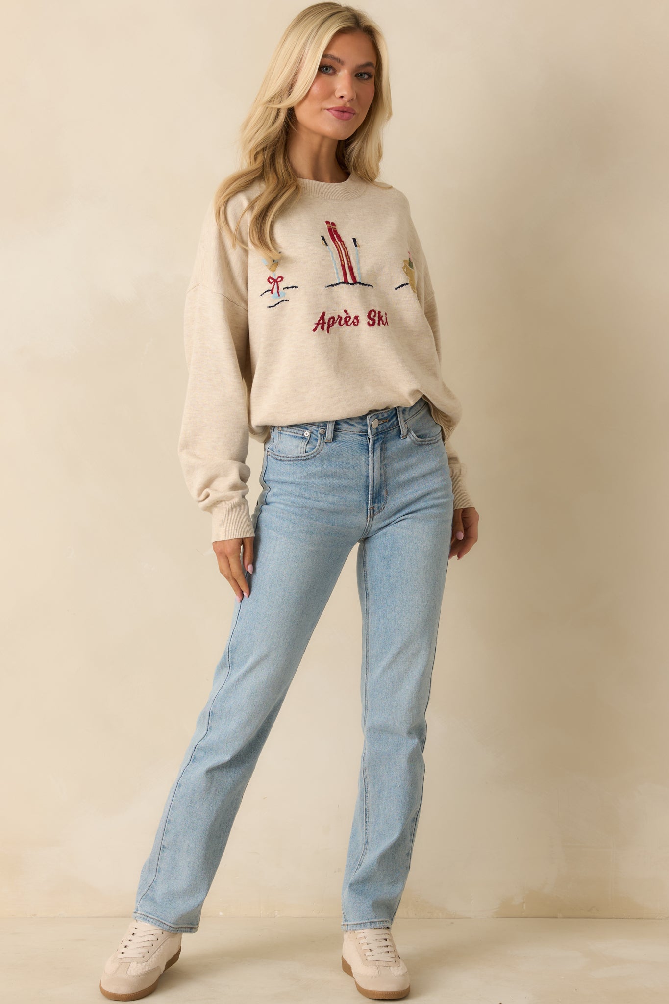 Angled front shot showing the sweater’s long sleeves, relaxed fit, and embroidered ski and cocktail motifs.