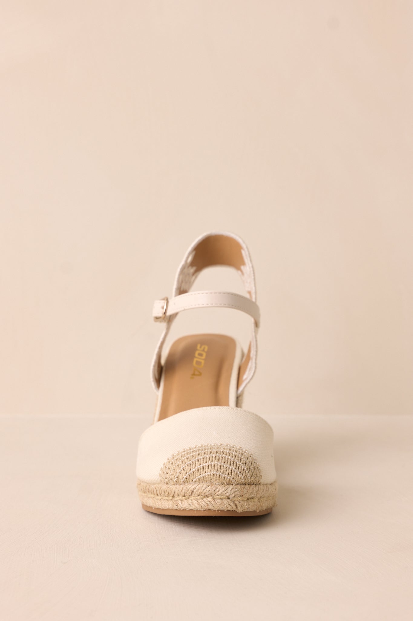 A slightly angled front shot displaying the rounded toe, toe piece, and the woven straw platform wedge heel.