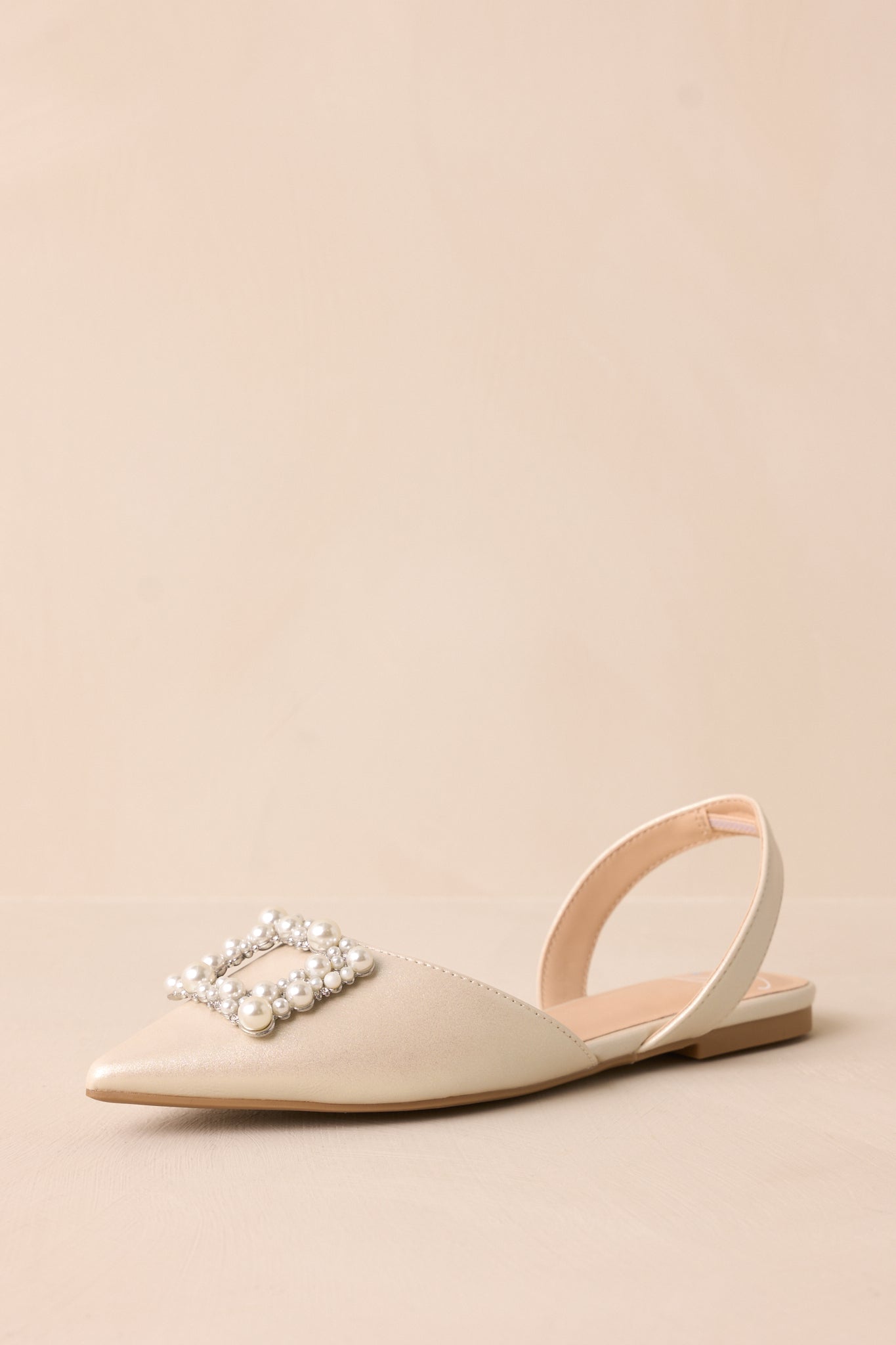 Angled front view of the flats, showcasing the pointed toe, slip-on structure, and the decorative rhinestone buckle with ivory pearls.