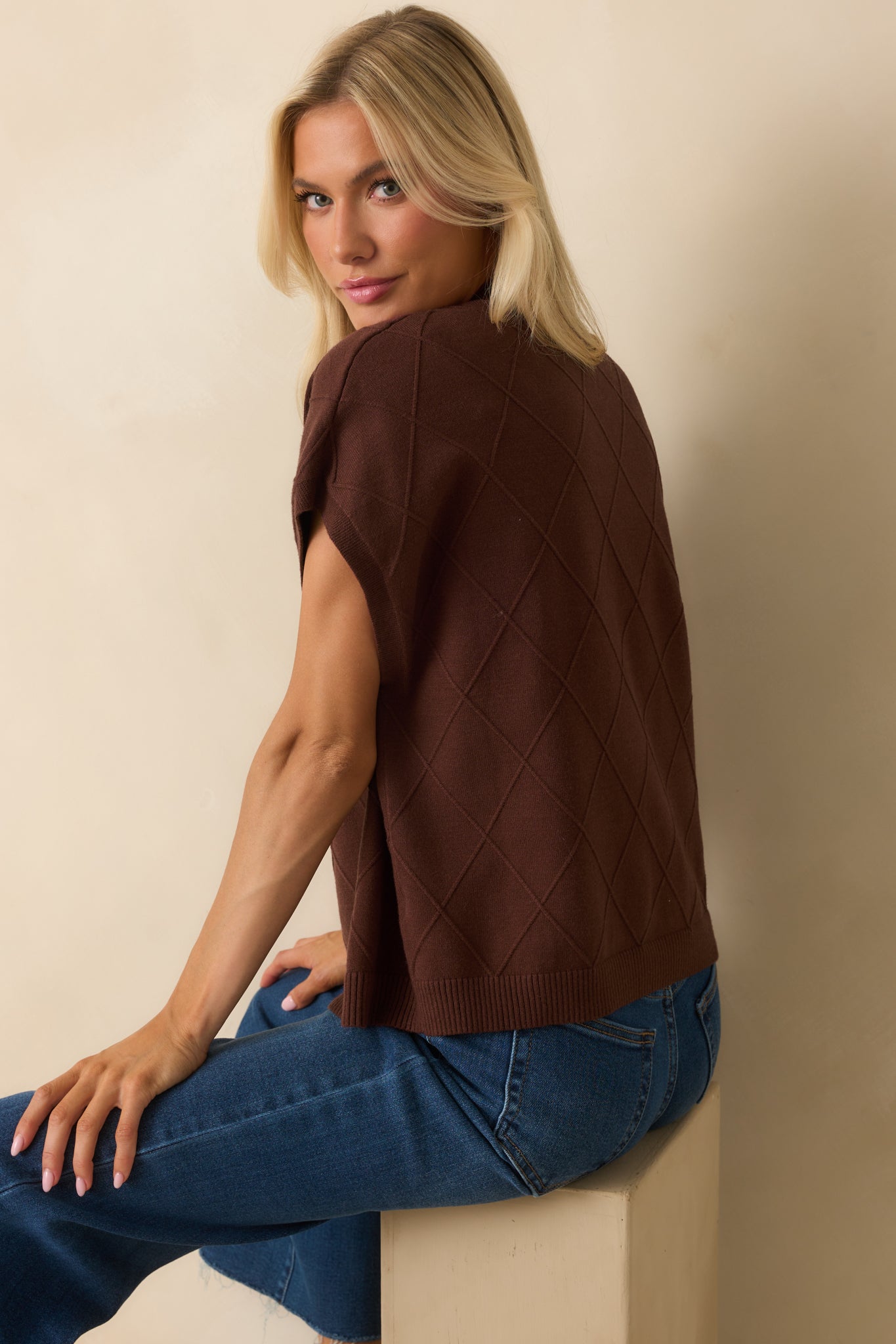 Angled rear view of brown sweater showing dolman sleeves, argyle stitch pattern, and straight hem from a side-back perspective.