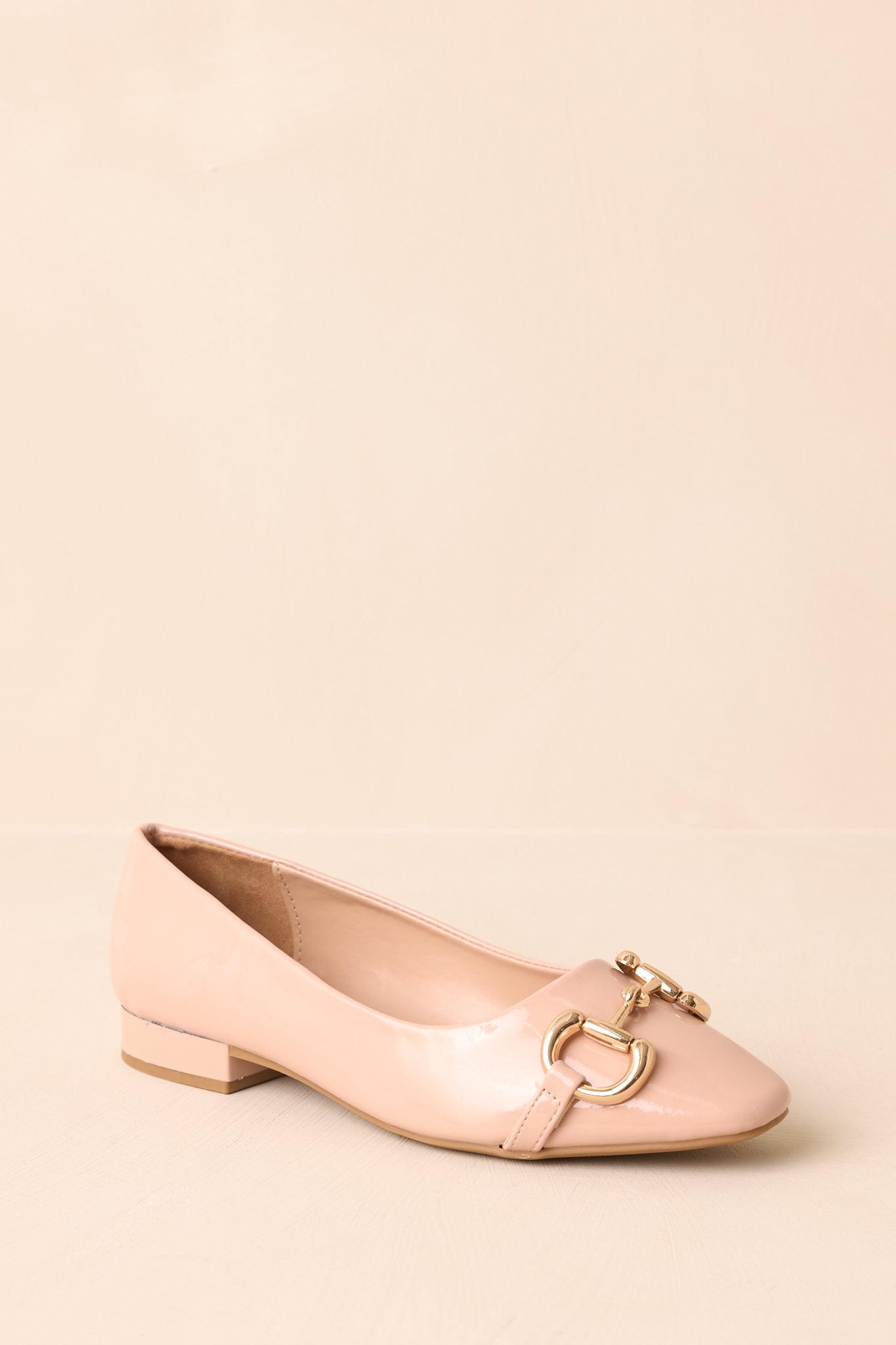 Angled top view of beige loafers, showcasing glossy patent finish and refined horsebit accent.