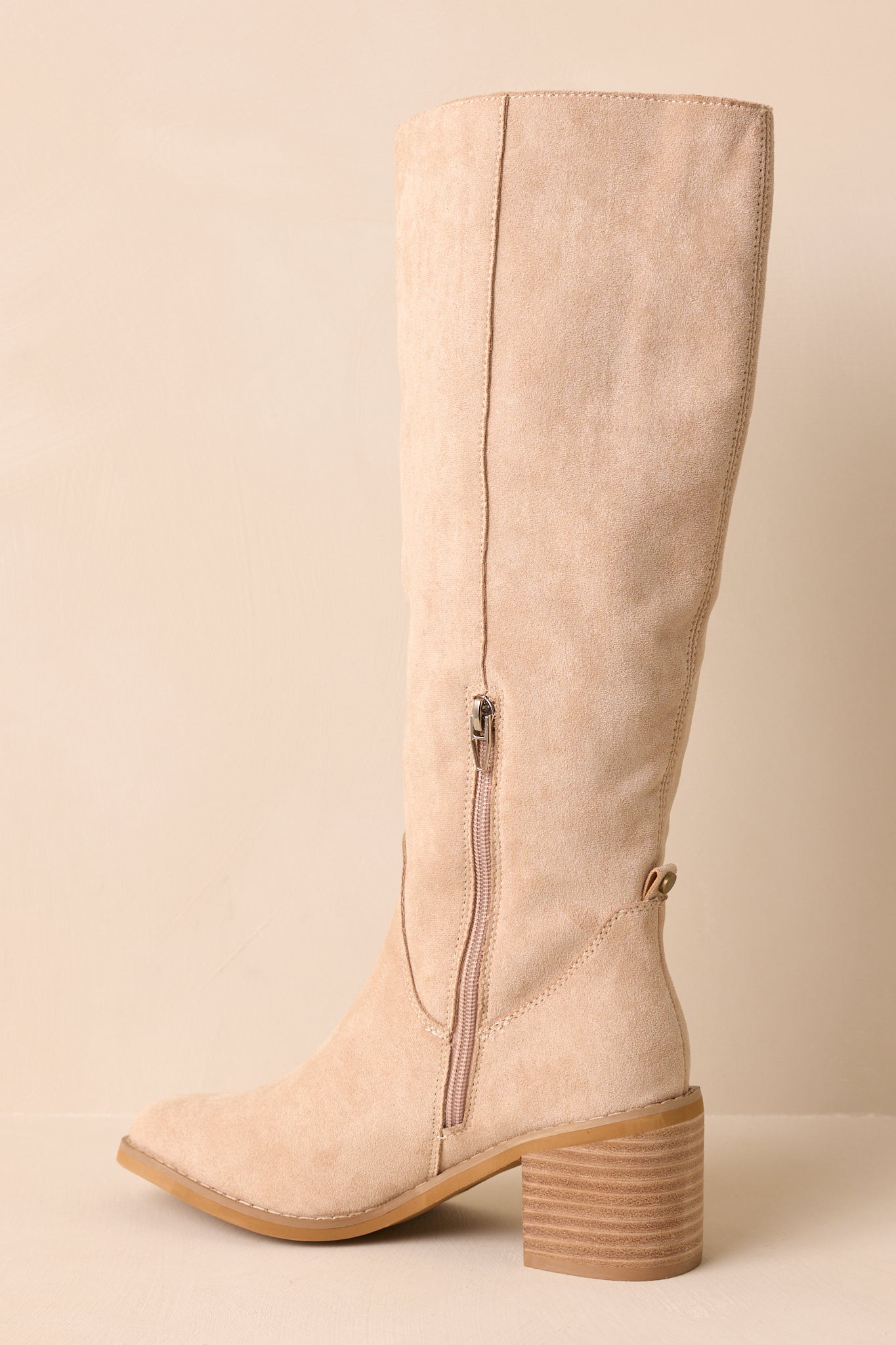 An angled back view of the beige boots highlighting the stacked block heel and inner side zipper closure.