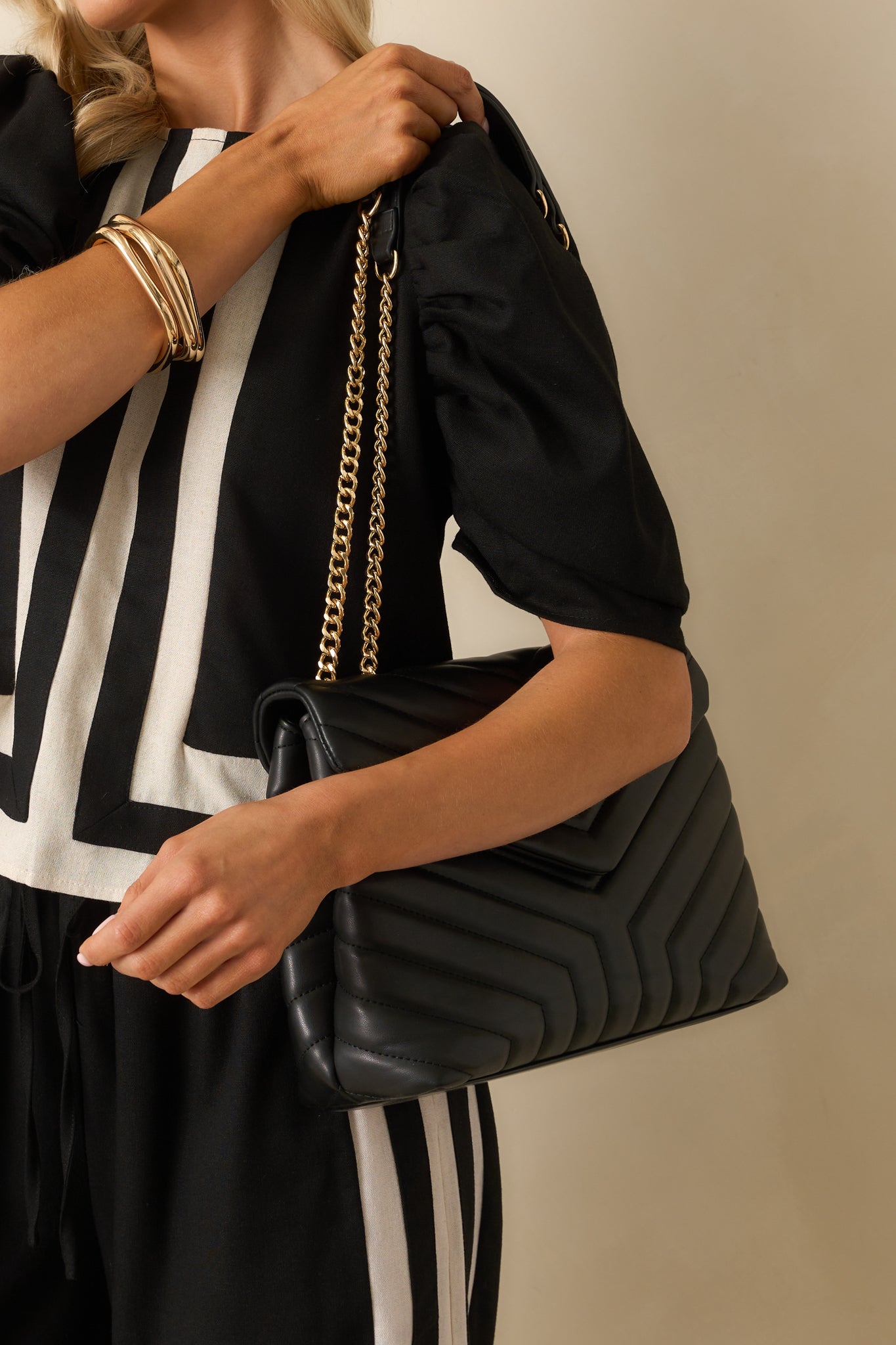 An angled view of the black quilted rectangular handbag with gold chain handles and faux leather grips.