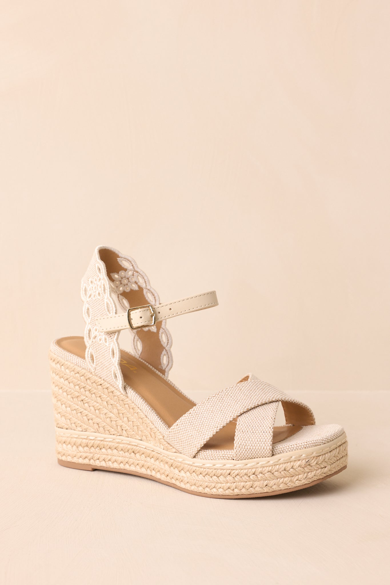 An angled front view of the wedge detailing the embroidered eyelet heel strap, capturing the stitching and airy pattern.