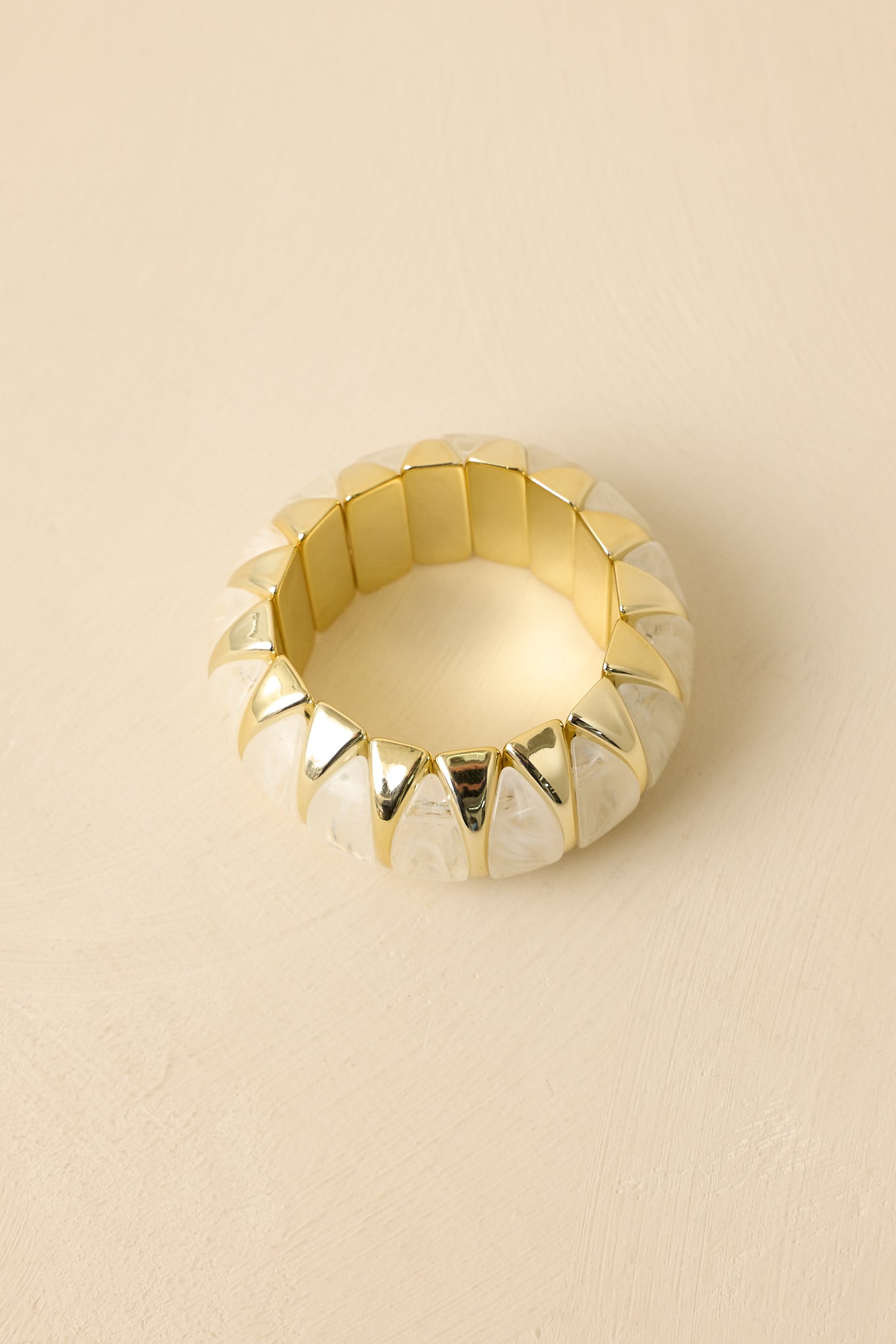 Angled view of sculptural bead bracelet against a neutral backdrop, emphasizing the curved gold links and dimensional design.
