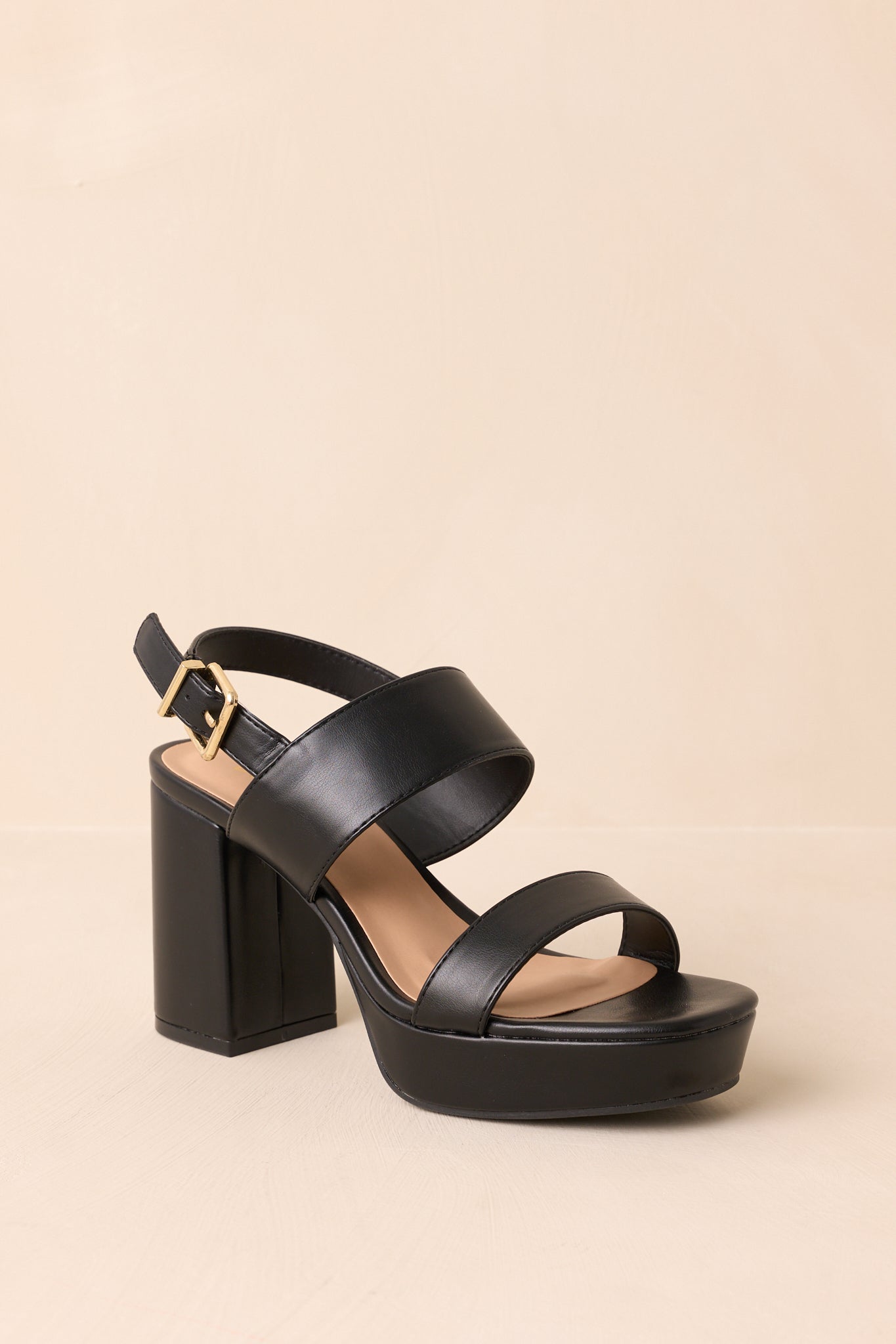 Angled view of the shoes against a beige background, showcasing the ankle strap and buckle closure.