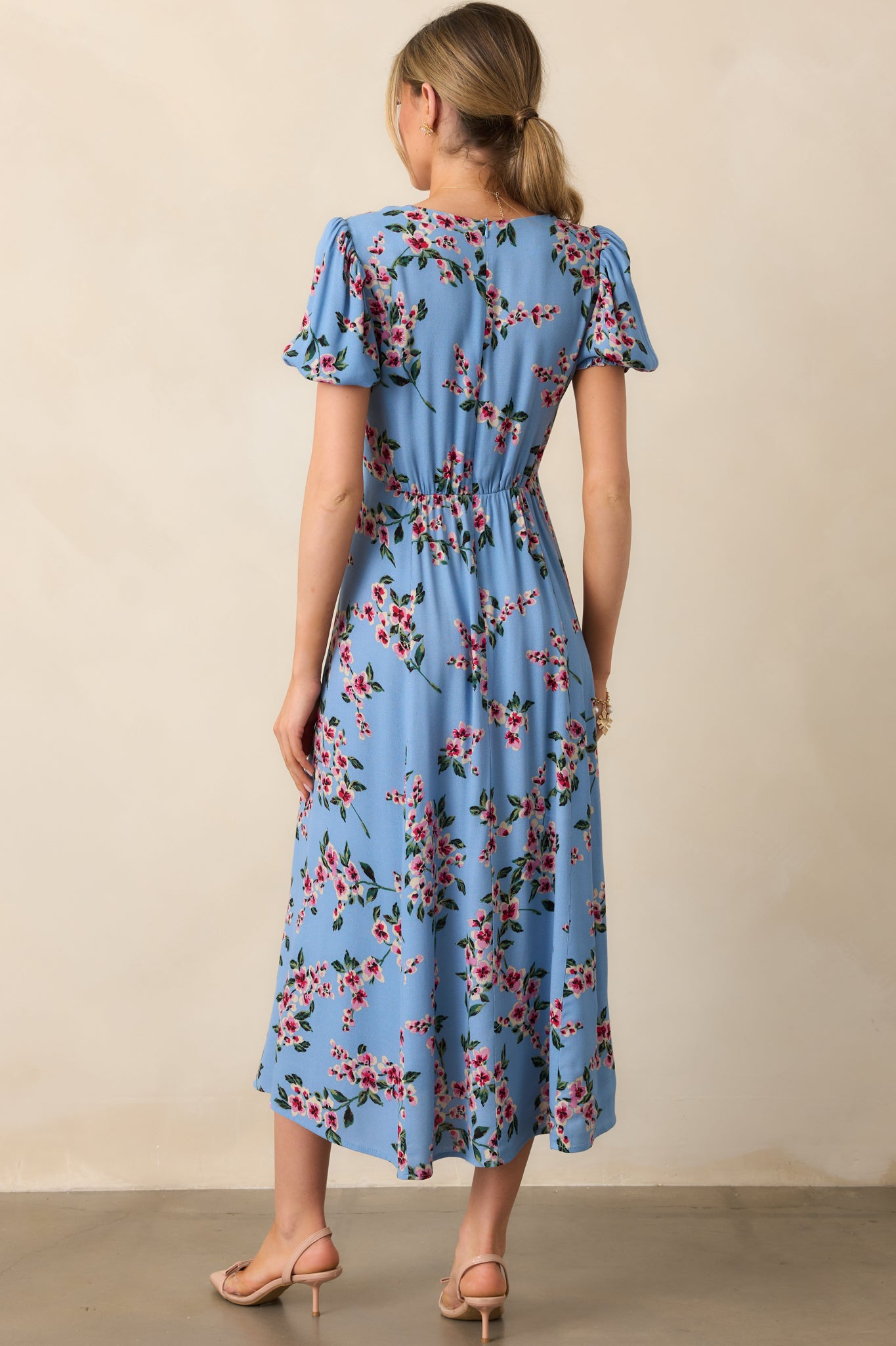 Back view of this floral midi dress dress featuring soft puff sleeves, a sweetheart neckline, and a delicate leg slit, all in a serene ash blue hue.