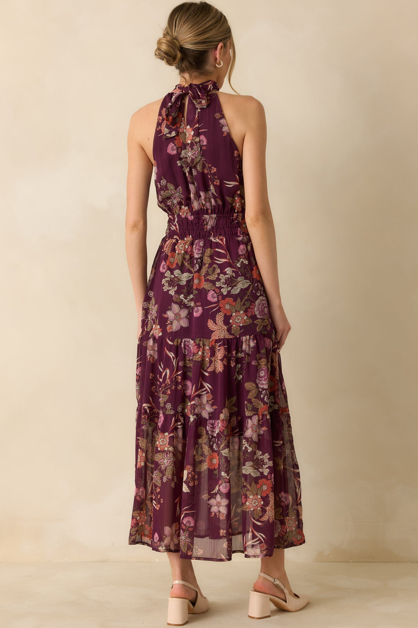 The back of the dress shows the adjustable halter tie, elasticized waist, and tiered maxi skirt with continuous floral print.