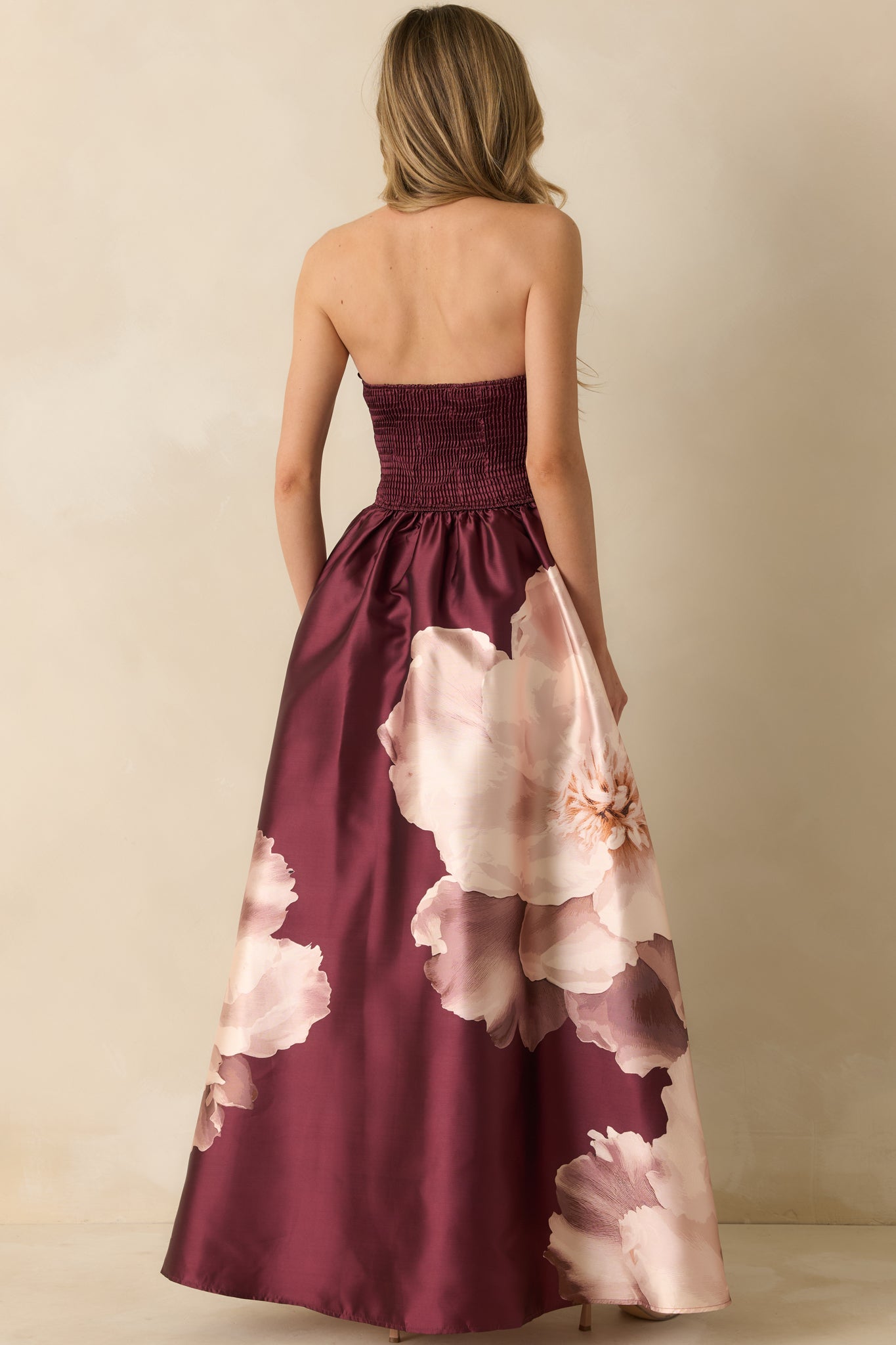 Back view of the burgundy floral maxi dress highlighting the smocked back panel and full skirt flow.