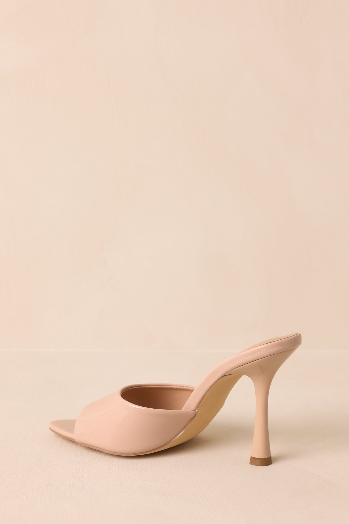 A back view of the beige mule heels highlighting the stiletto heel and streamlined slip-on design.