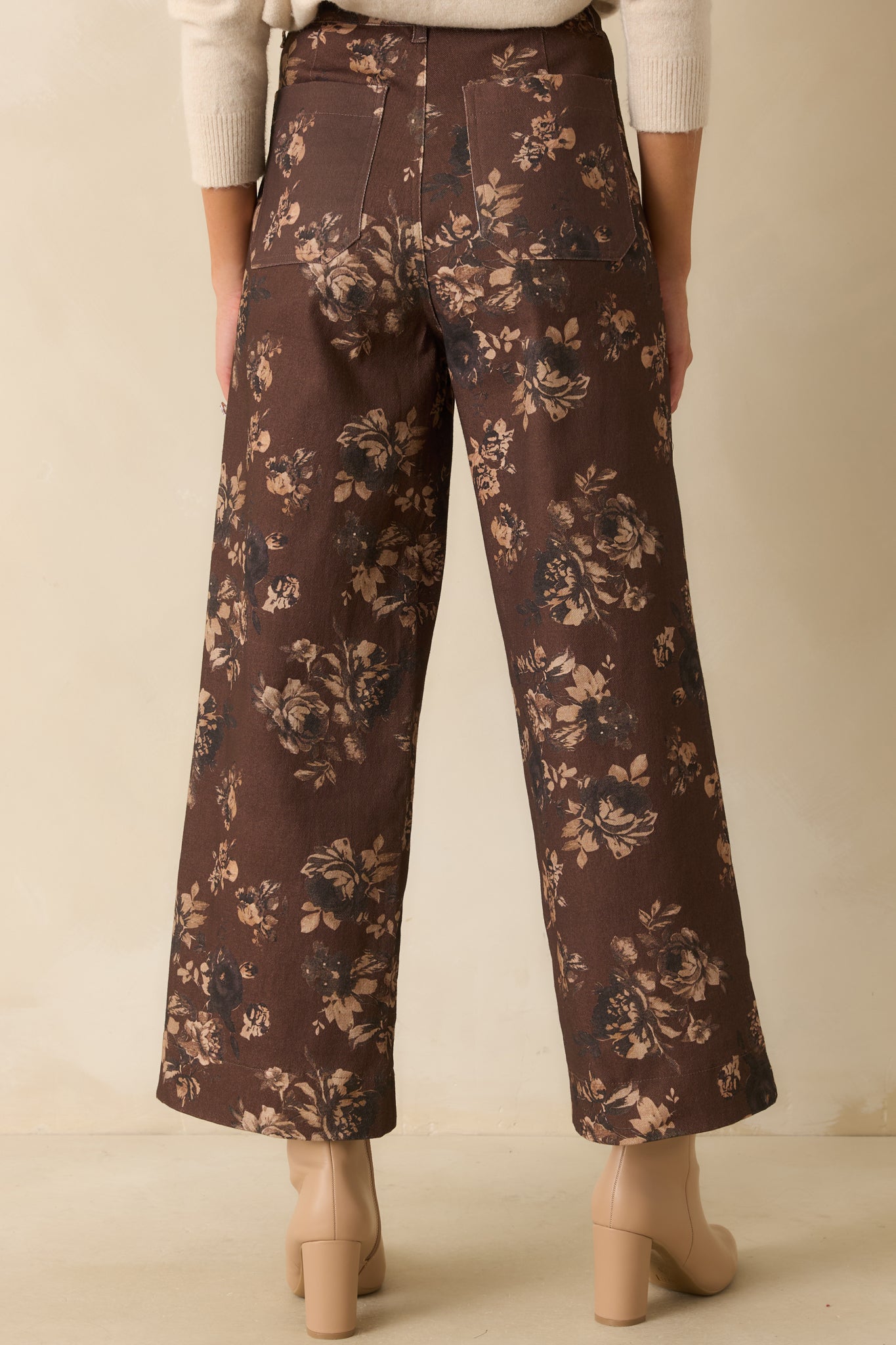 A back view of the chocolate brown jeans featuring functional back patch pockets, belt loops, and wide leg design with allover floral print.