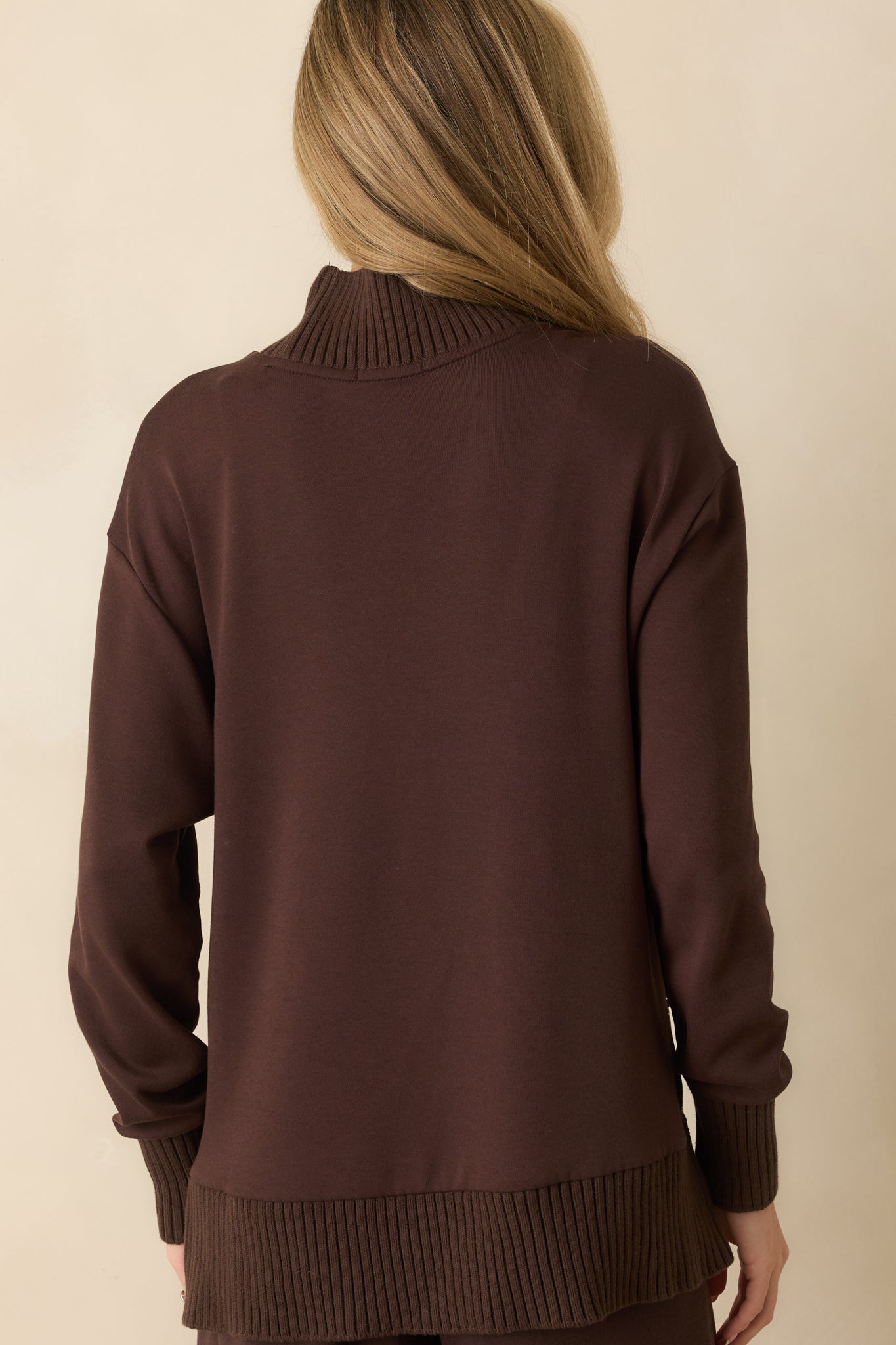 A back view of the dark brown sweater featuring an oversized silhouette, long sleeves, and ribbed hem and cuffs.