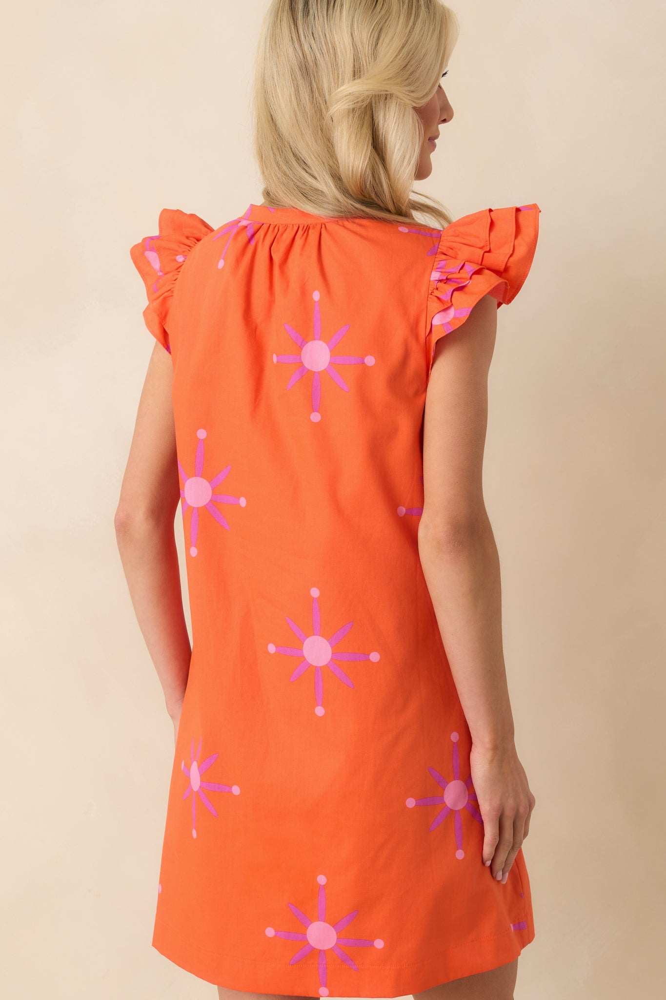 Back view of the mini dress displaying the continuation of the floral print and the flow of the orange-lined fabric.