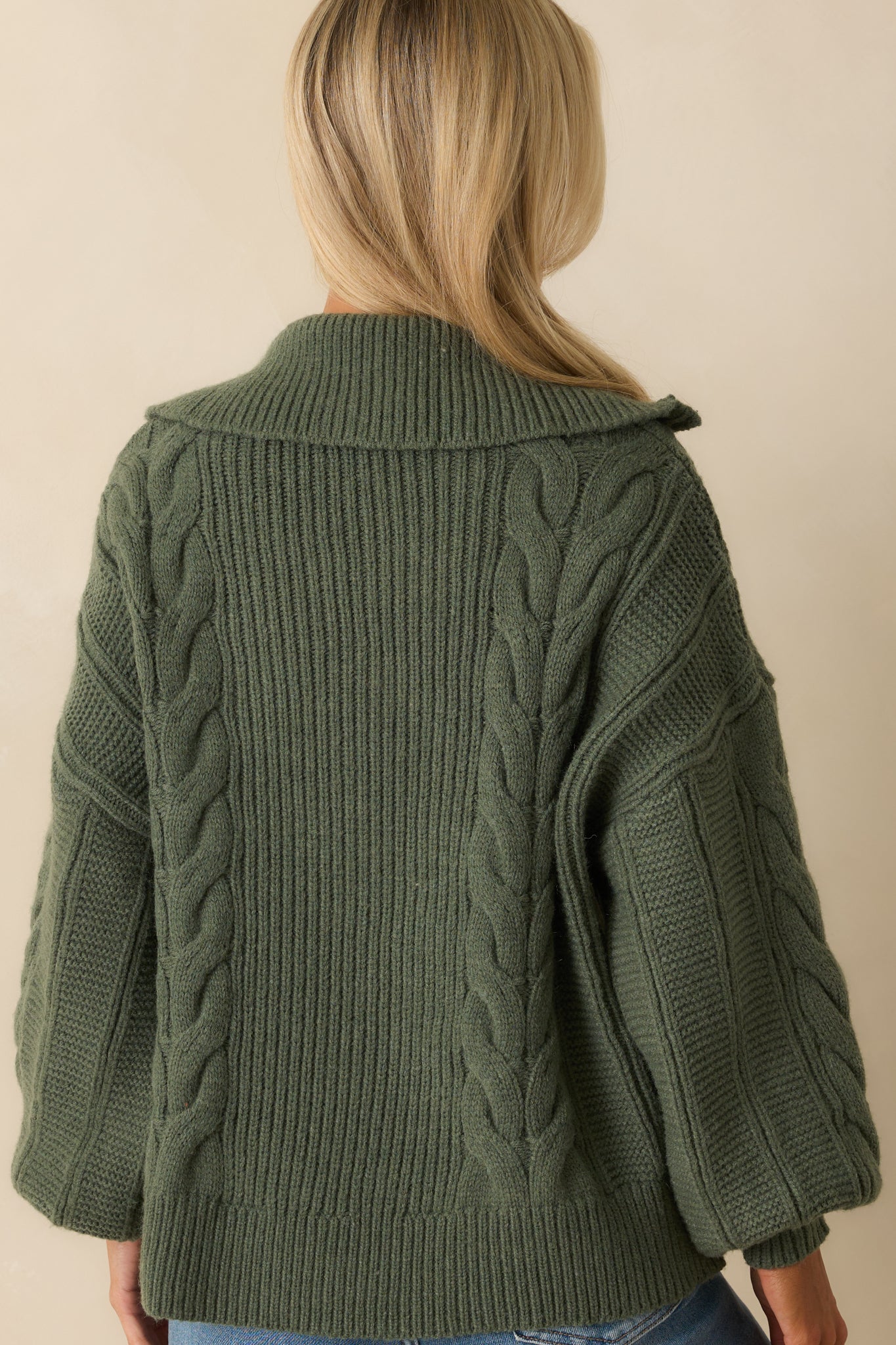 A back view of the sweater displaying the relaxed fit, drop shoulders, and continuous cable knit fabric.