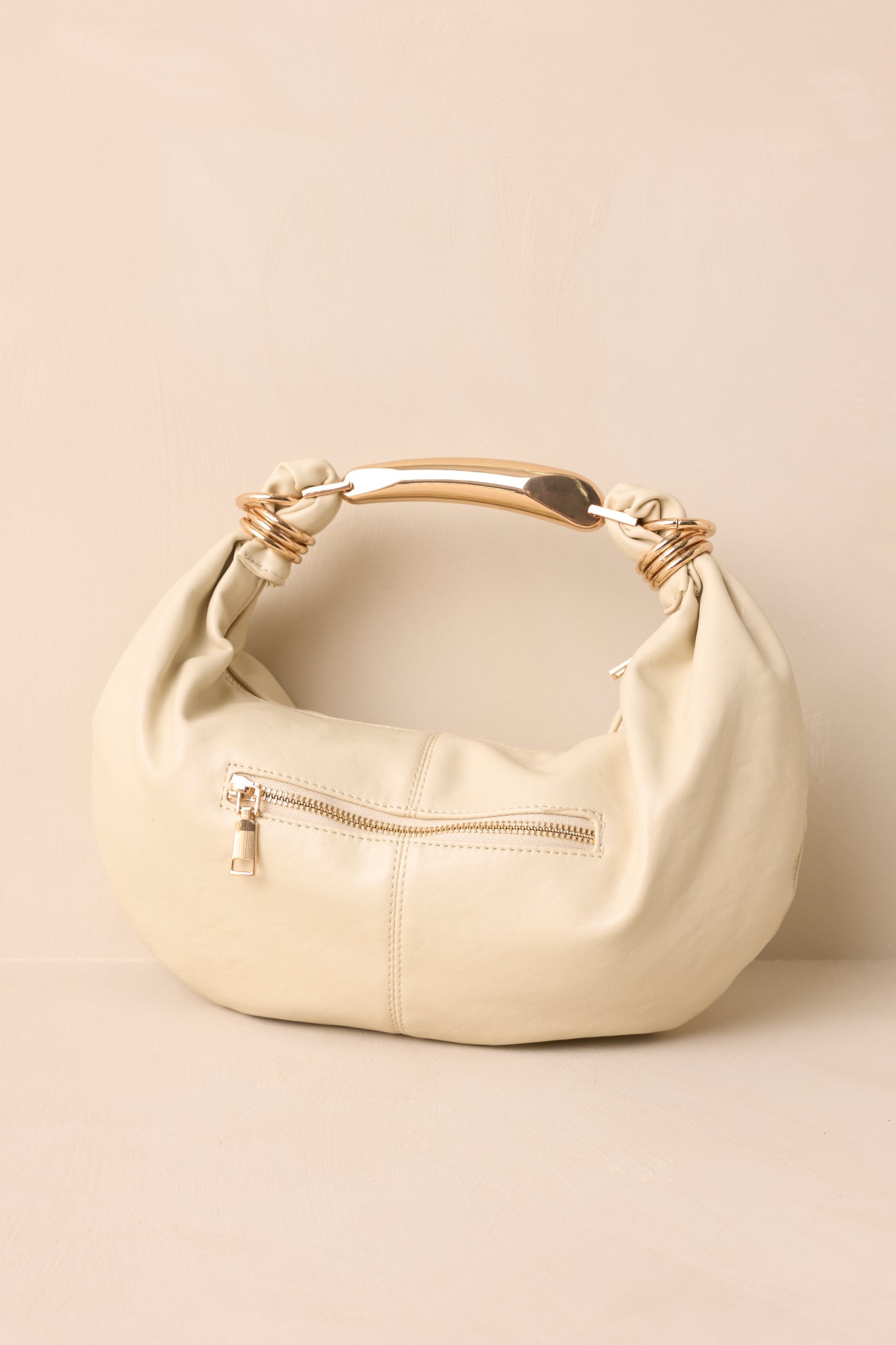 A back view of the handbag displaying the smooth ivory faux leather, single zipper, and slouchy crescent shape.