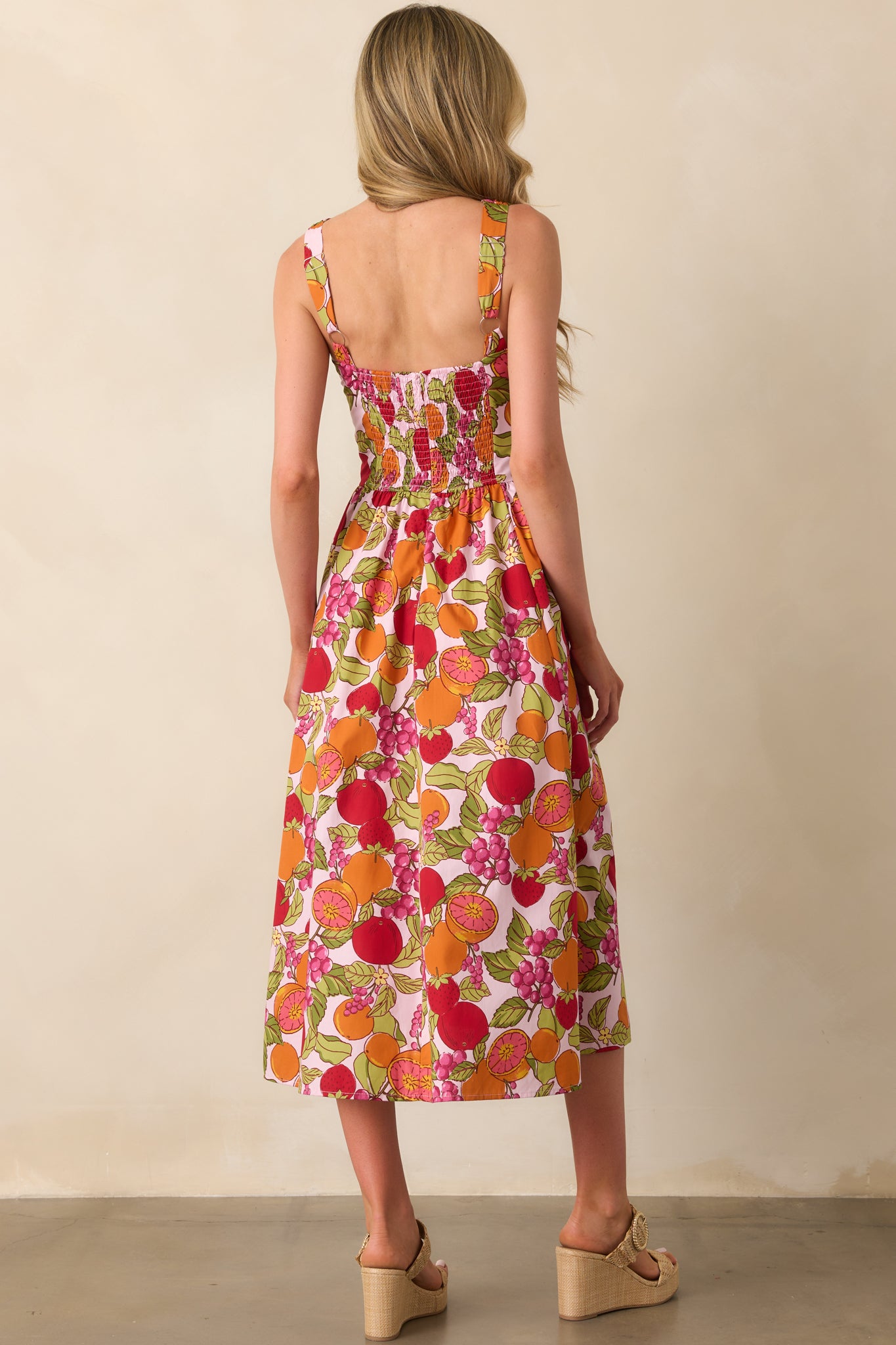 Back view of the dress displaying the smocked panel, hidden back zipper, and the continuation of the multicolor fruit print.