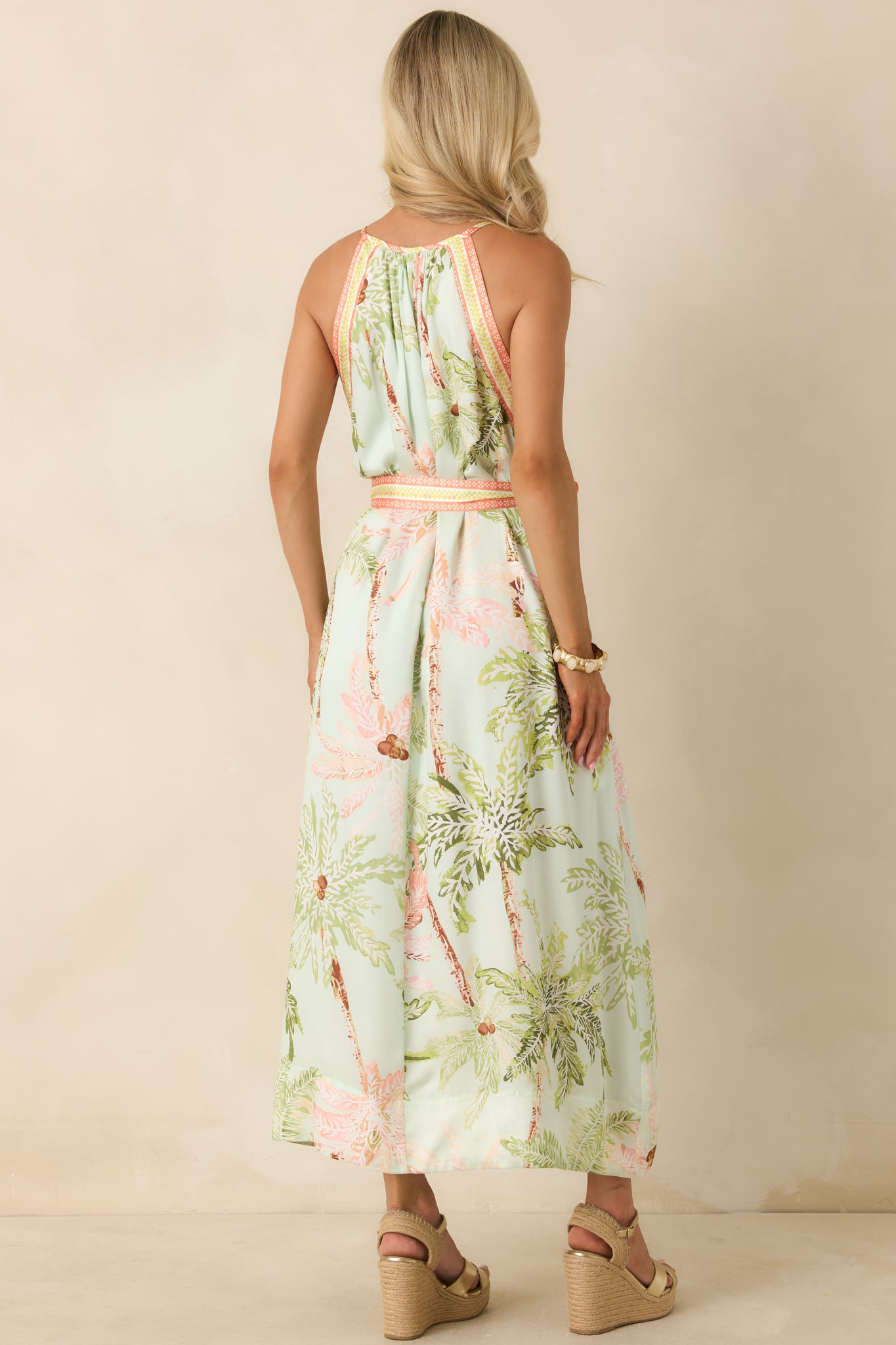 Back view of the flowing maxi dress featuring a sleeveless design, waist-defining sash, and continuous watercolor-inspired palm print.