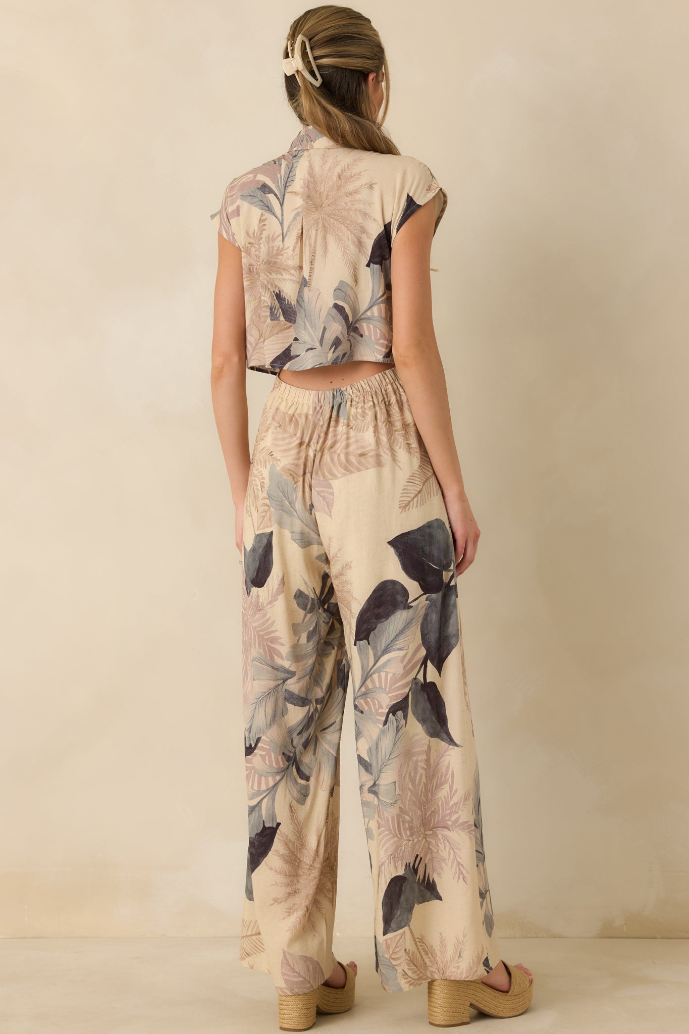 Back view of beige tropical print jumpsuit featuring open back design and elastic waistband for shaping.
