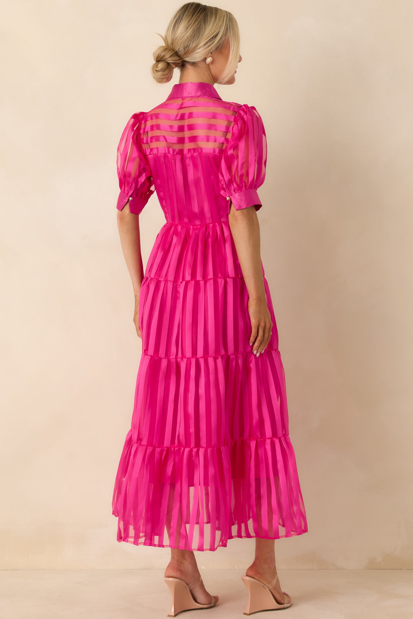 Rear of the fuchsia pink maxi dress showing a smooth back panel, tiered skirt, and gentle flow of the sheer striped fabric.