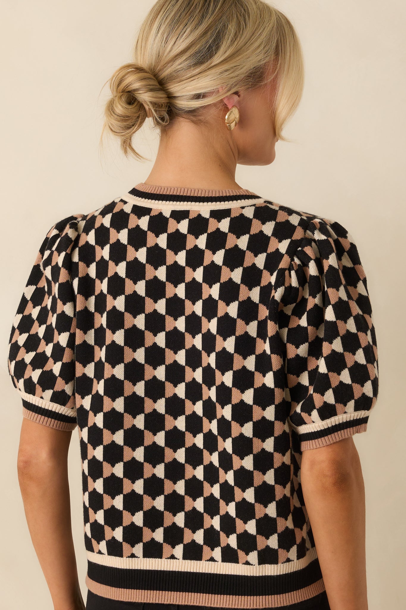 Rear view of black and beige geometric print knit top showing short puff sleeves, ribbed hem, and cropped fit.