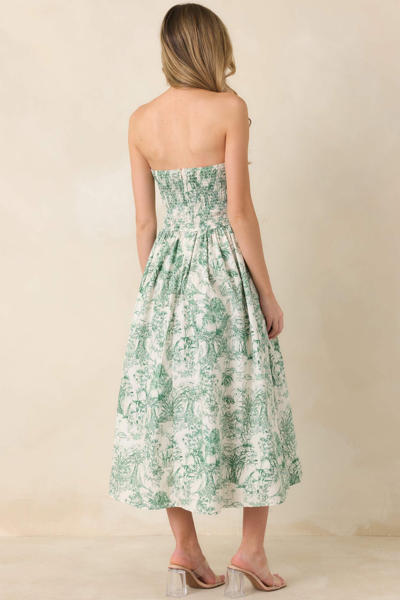 Back view of green toile midi dress showing smocked back, discrete zipper, and pleated skirt drape.