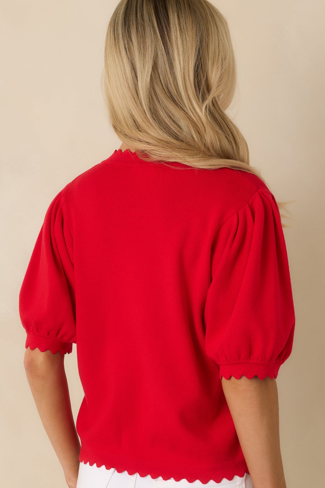 Back view of the red knit cardigan highlighting the clean back panel, short puff sleeves, and scalloped hem detail.