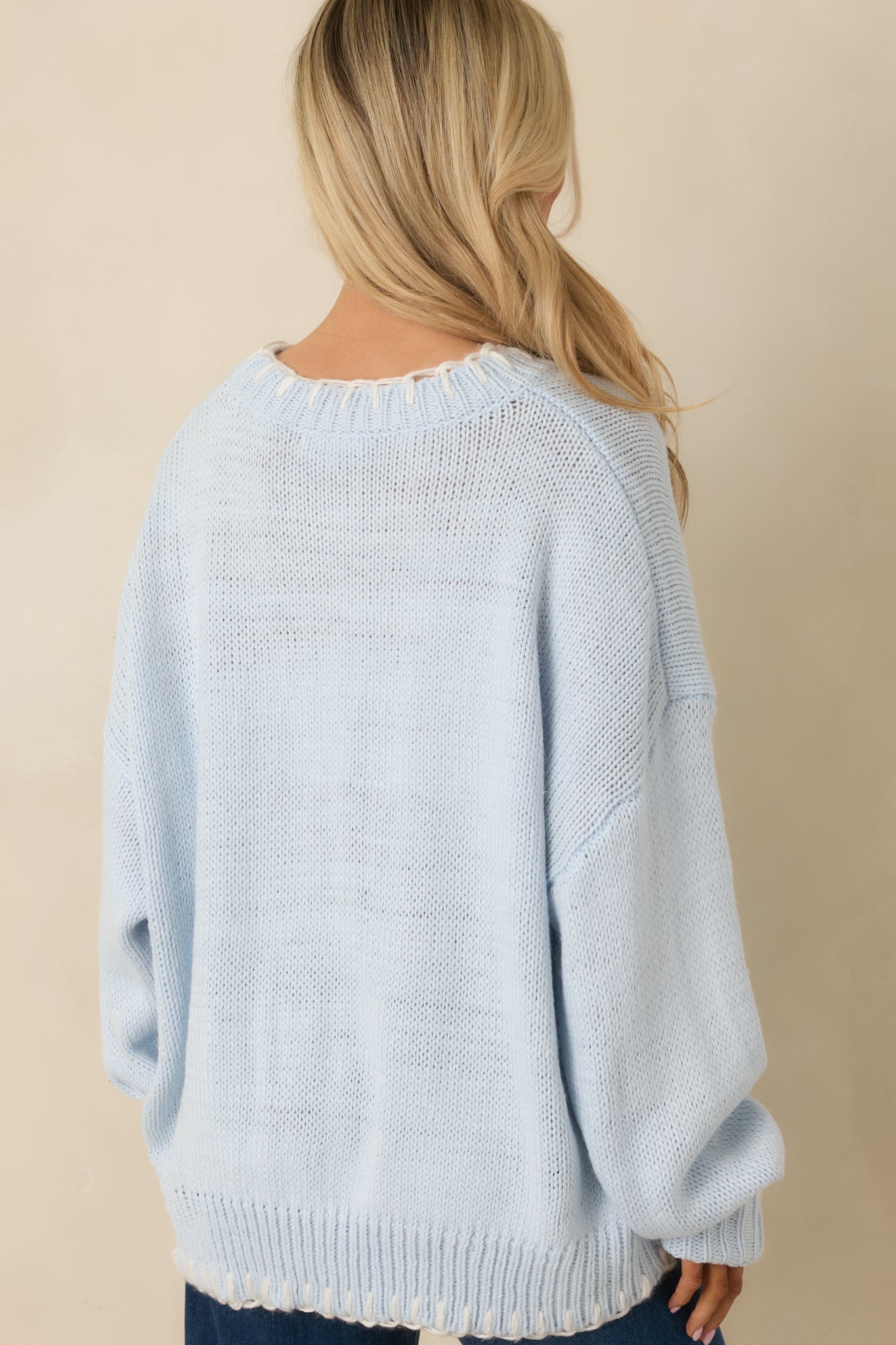 Back view of the light blue knit sweater highlighting the smooth knit fabric, long sleeves, and relaxed silhouette.