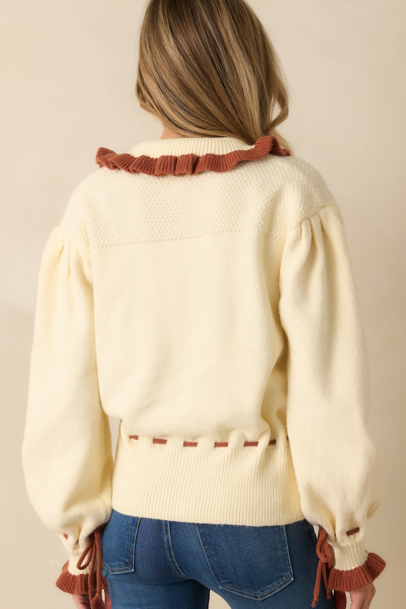 Back view of ivory button-up cardigan showing long puff sleeves, rust tie cuffs, and relaxed fit.