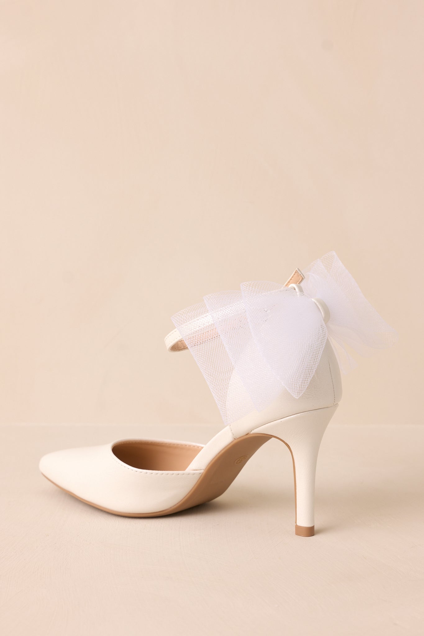 Back view showing the large layered ivory lace bow, thin heel, and ankle strap with silver buckle.