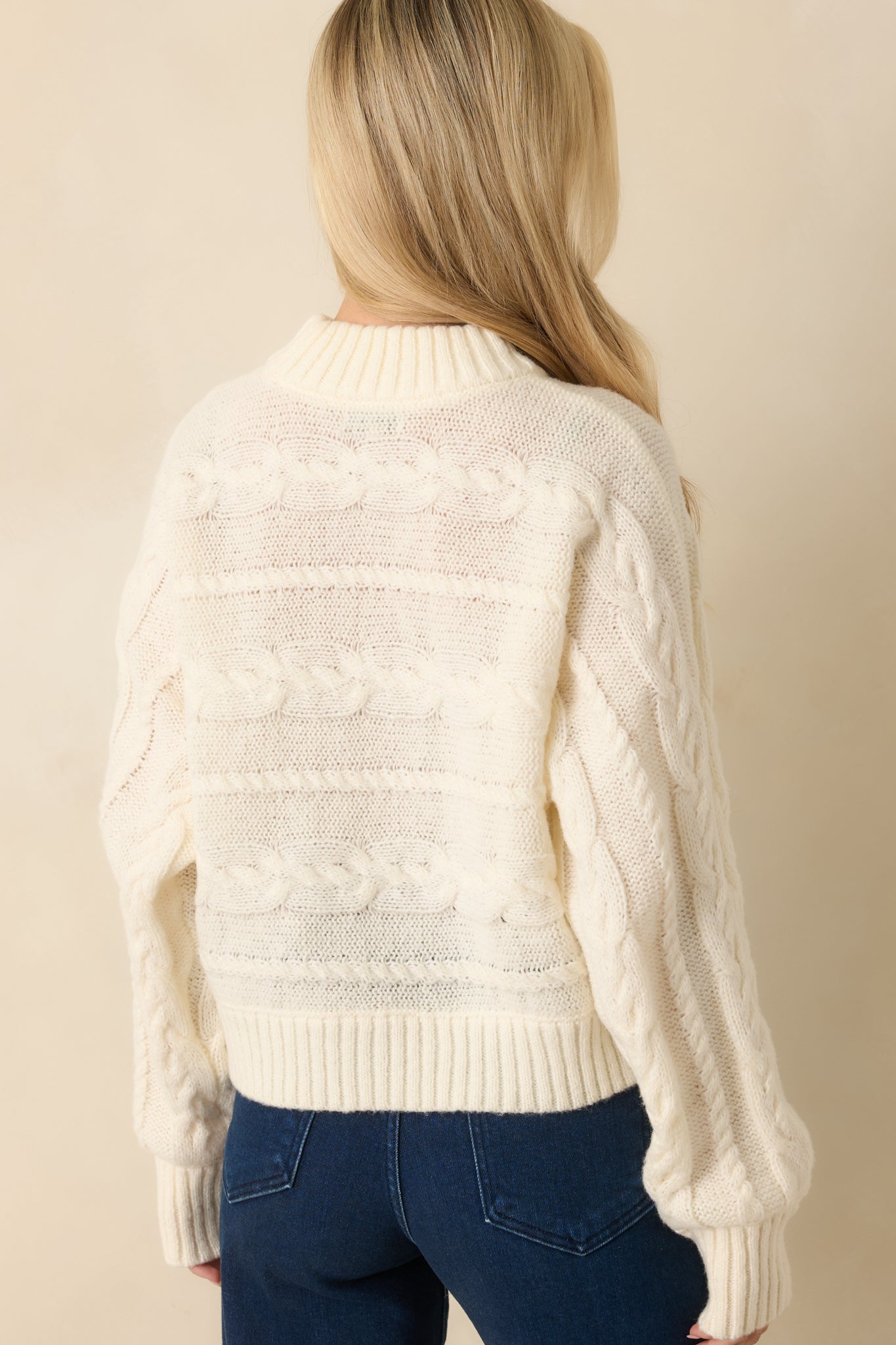 Back view of the ivory sweater showing cable detailing and ribbed hem finish.