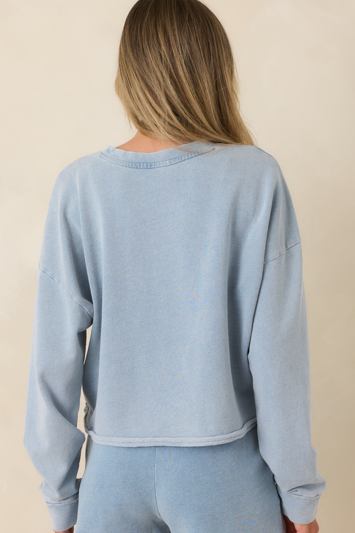 Back view of the light denim blue sweatshirt highlighting the relaxed fit and raw-edge hem.