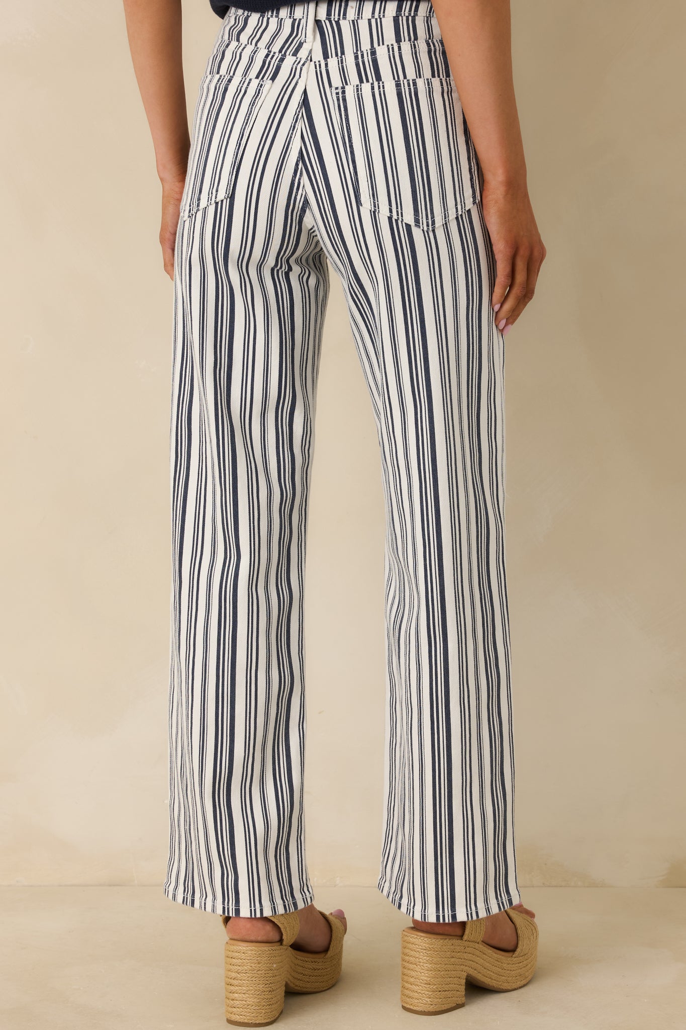 Navy striped wide-leg pants displaying the high-rise waistband and relaxed straight-leg silhouette from the rear.