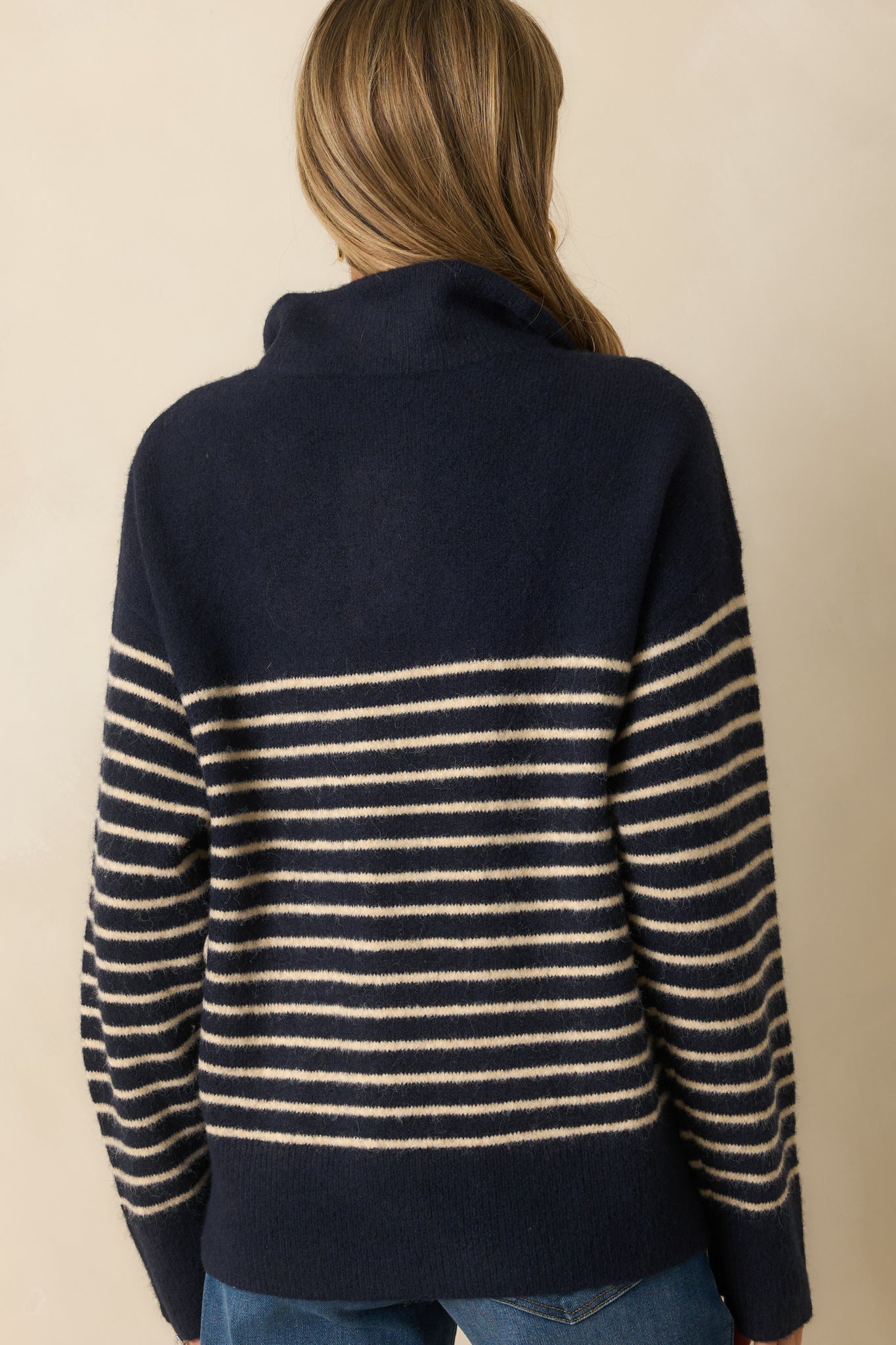 A back view of the navy sweater featuring horizontal ivory stripes across the back and long sleeves with a ribbed hem.