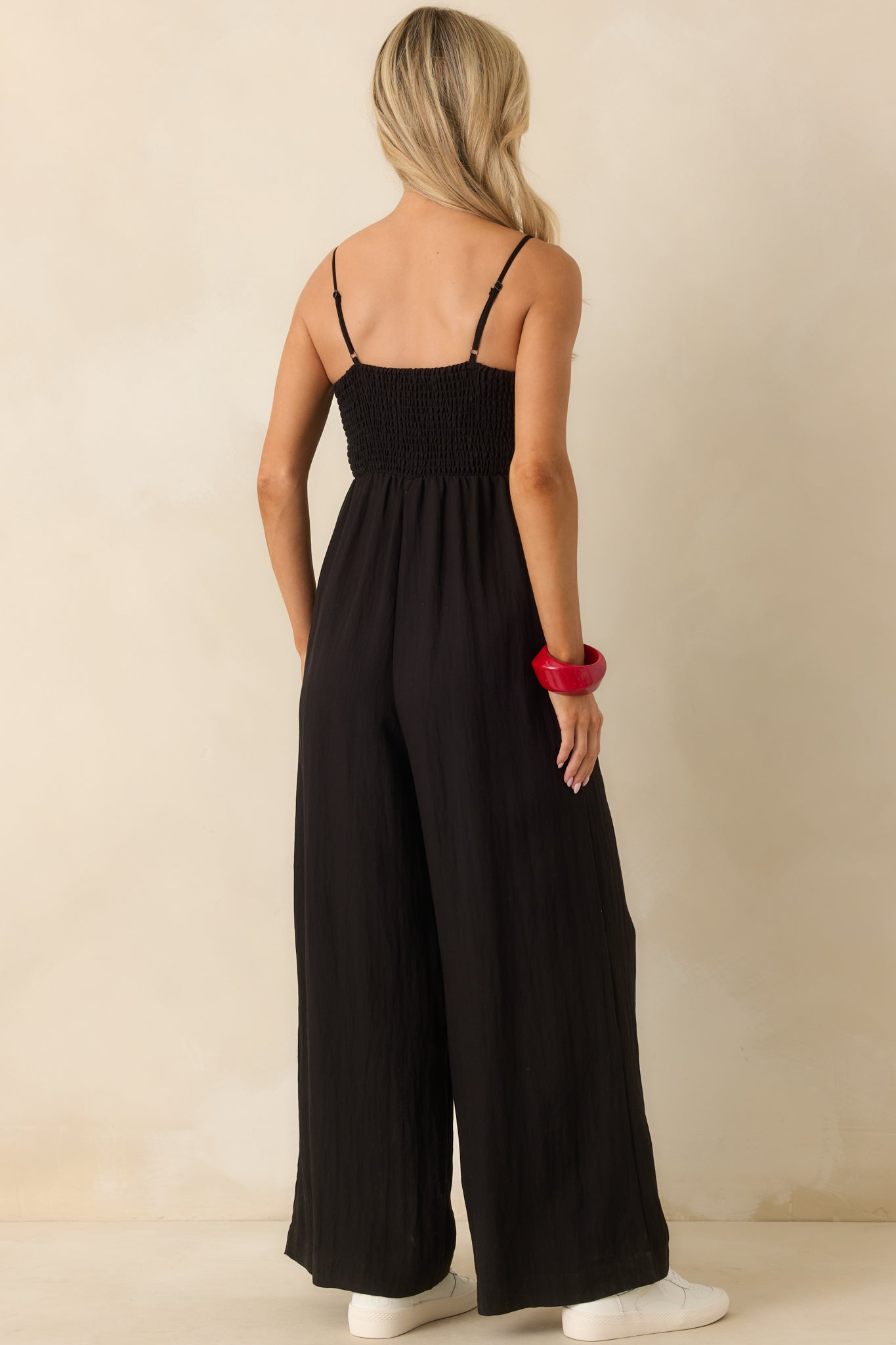 Back view of the black jumpsuit, featuring adjustable straps, smocked paneling, and wide ankle-length legs.