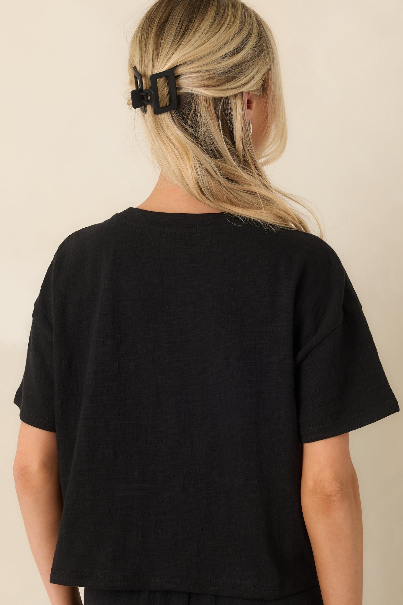 Back view of black textured cropped top showcasing boxy silhouette and short sleeve design.