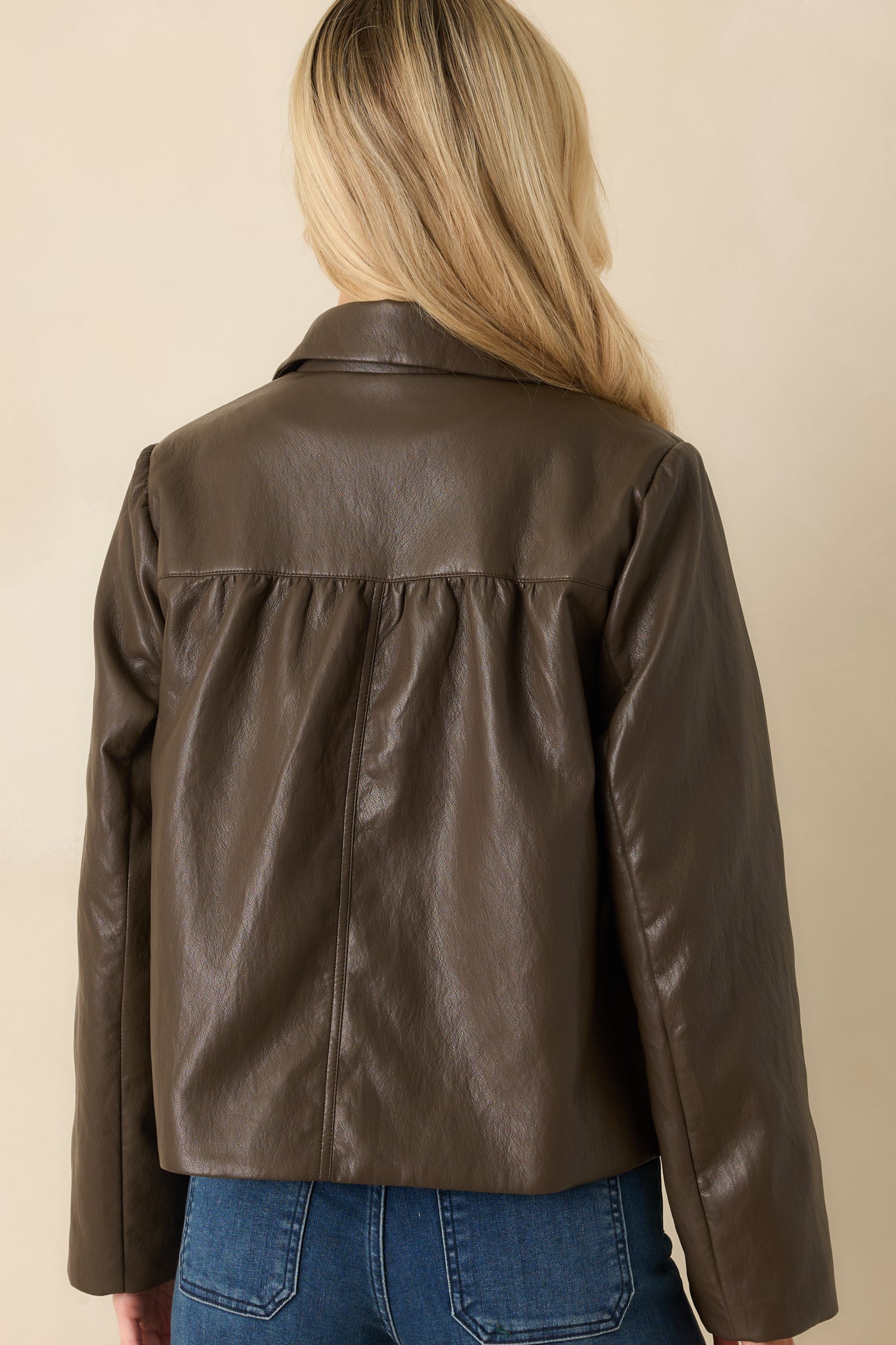 Back view of dark brown faux leather jacket showing straight hem, long sleeves, and smooth finish.