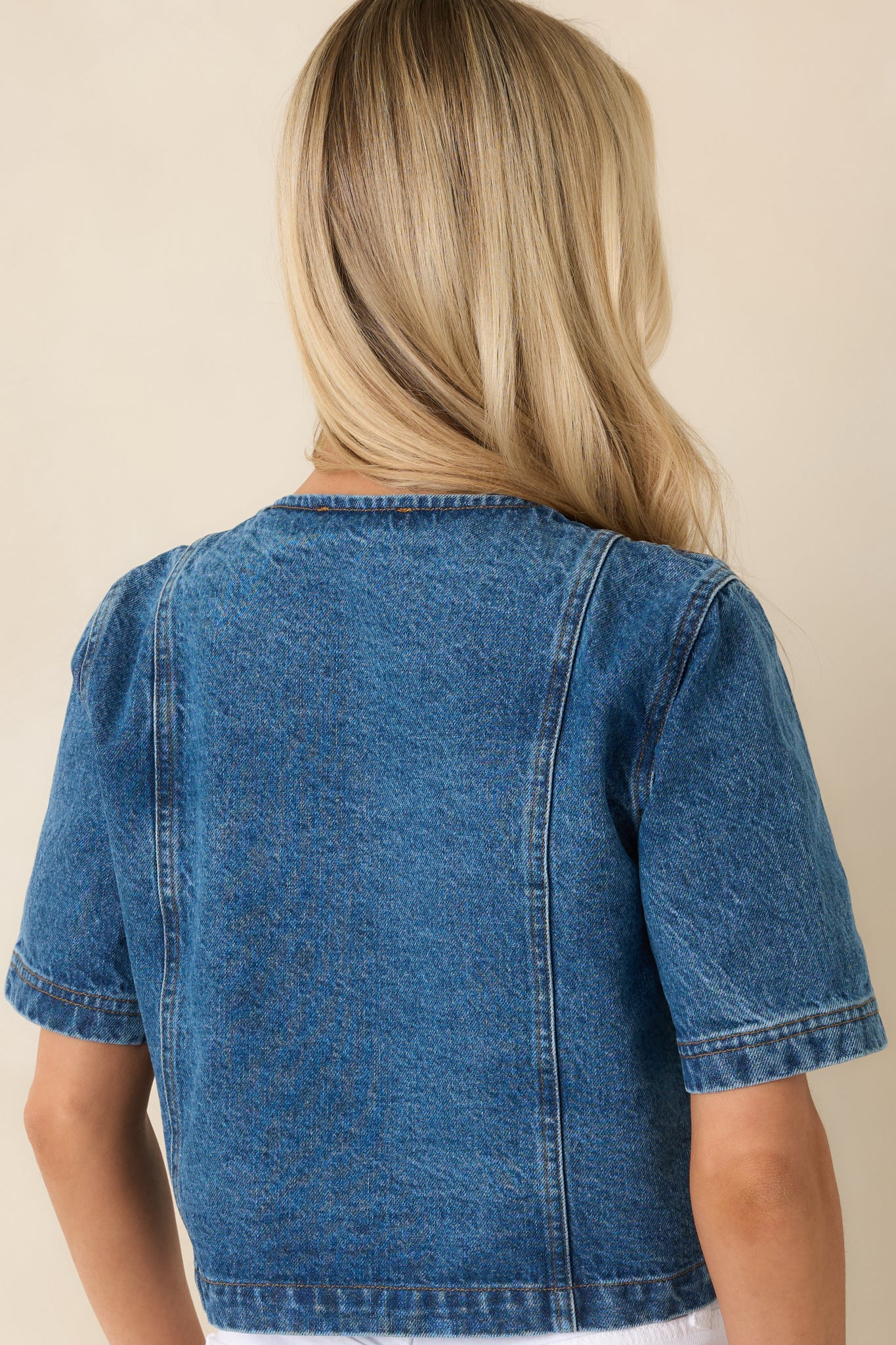 Back view of cropped medium wash denim top featuring a clean, structured silhouette and short sleeves