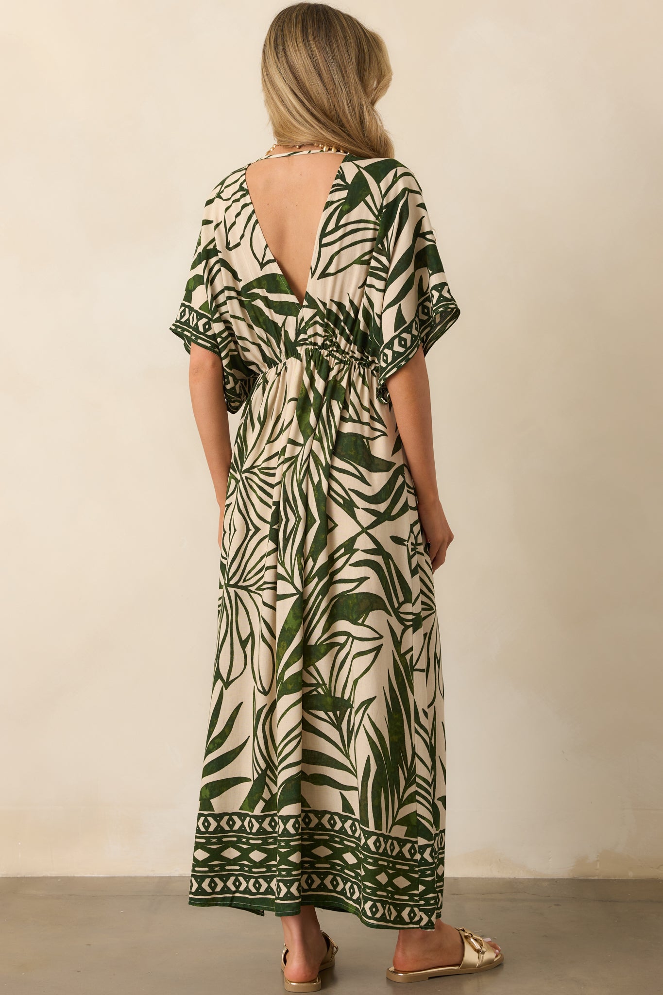 Back view of the green and beige palm leaf print maxi dress, showcasing the open V-back, kimono-style sleeves, and the elastic waistband.