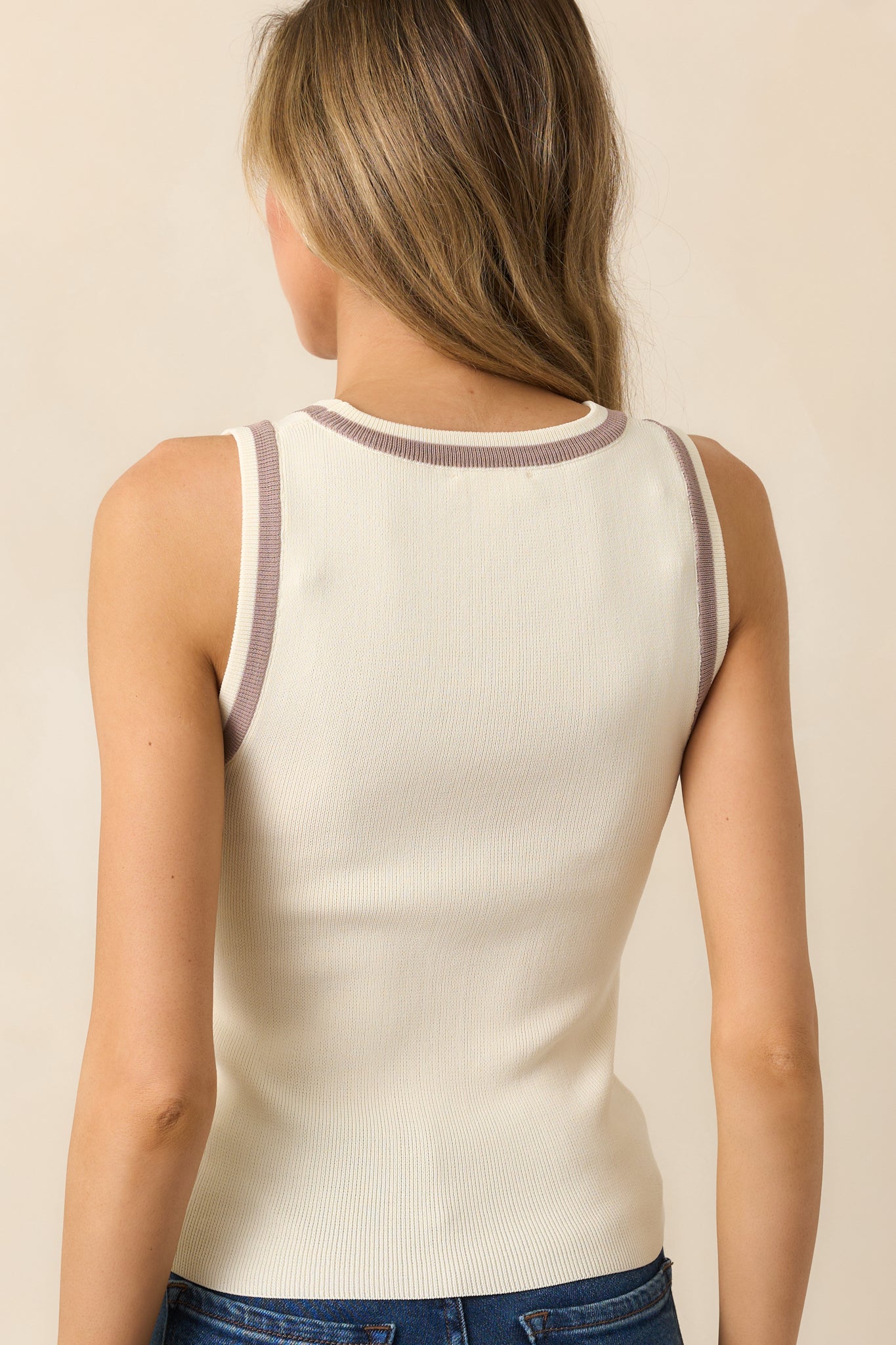 Back view of the ivory tank top with a bodycon fit and sleeveless design, finished with brown hem details for added style.
