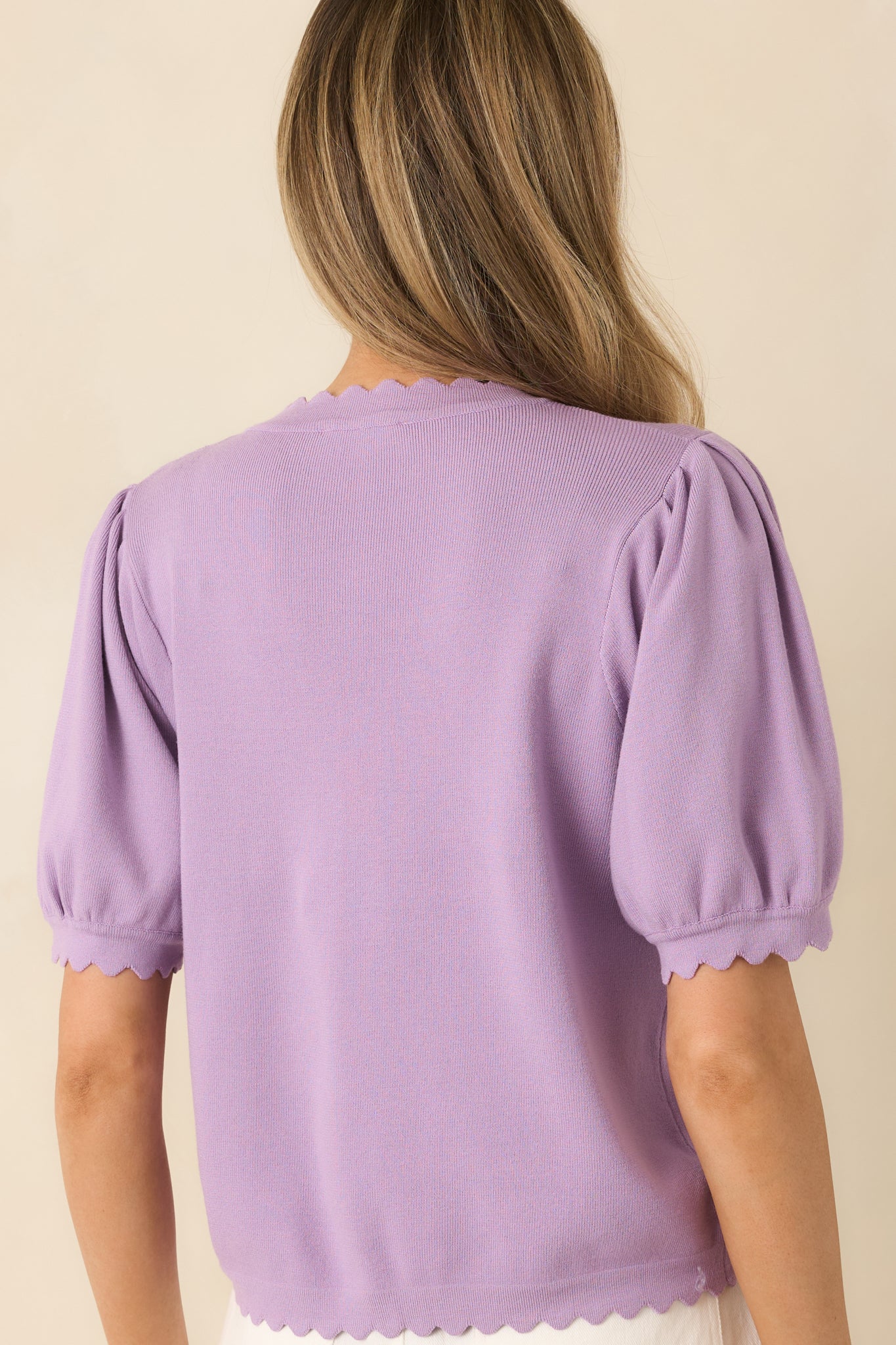 Back view of lavender knit cardigan highlighting short puff sleeves and scalloped hem detail.