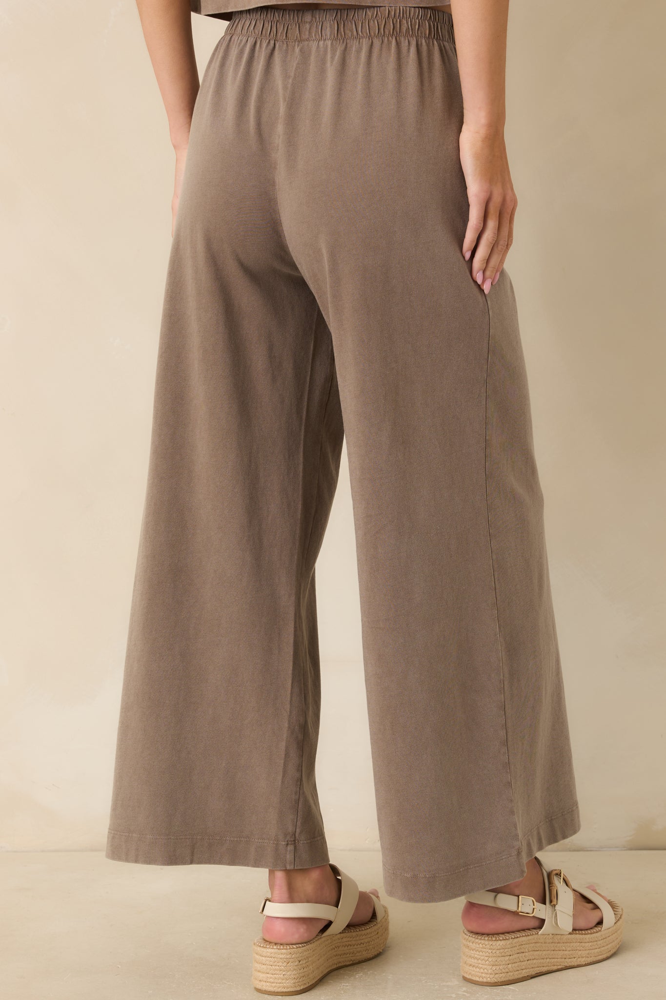 Back view of the dark taupe pants featuring a relaxed fit, elastic waistband, and wide leg silhouette in soft cotton jersey fabric.