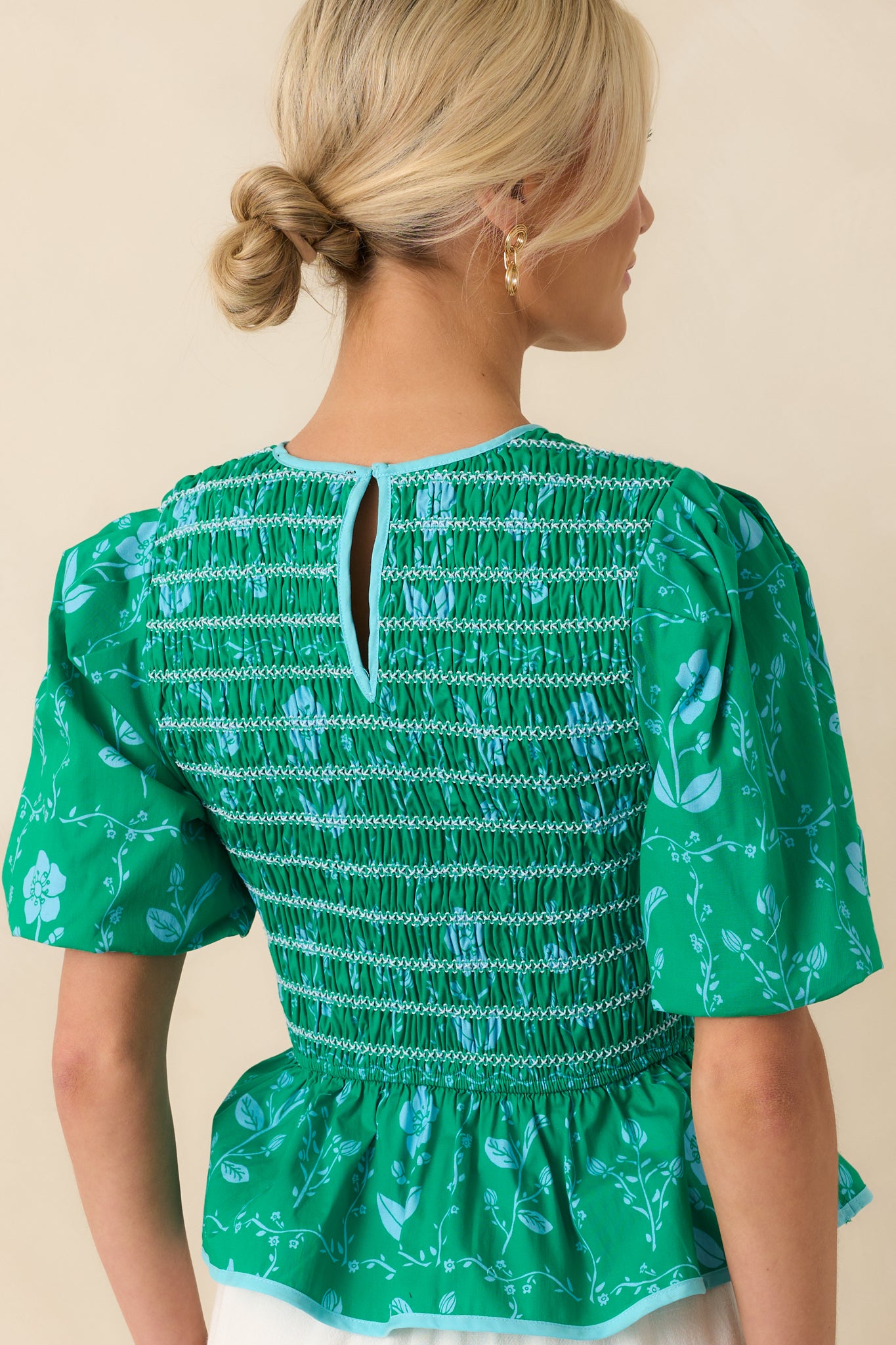 Back view of the top showing the keyhole closure, puff sleeves, and peplum flare from behind.