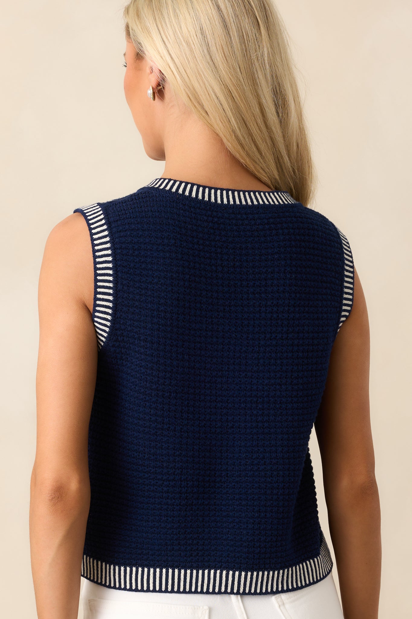 Back view of the navy sweater vest, showing the clean design with a scoop neckline, functional waist pockets, and stylish white stripe hems.