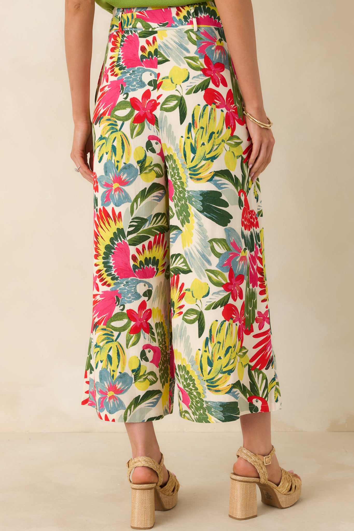 Back view of tropical print pants showing high-rise fit, wide-leg silhouette, and colorful parrot and floral pattern